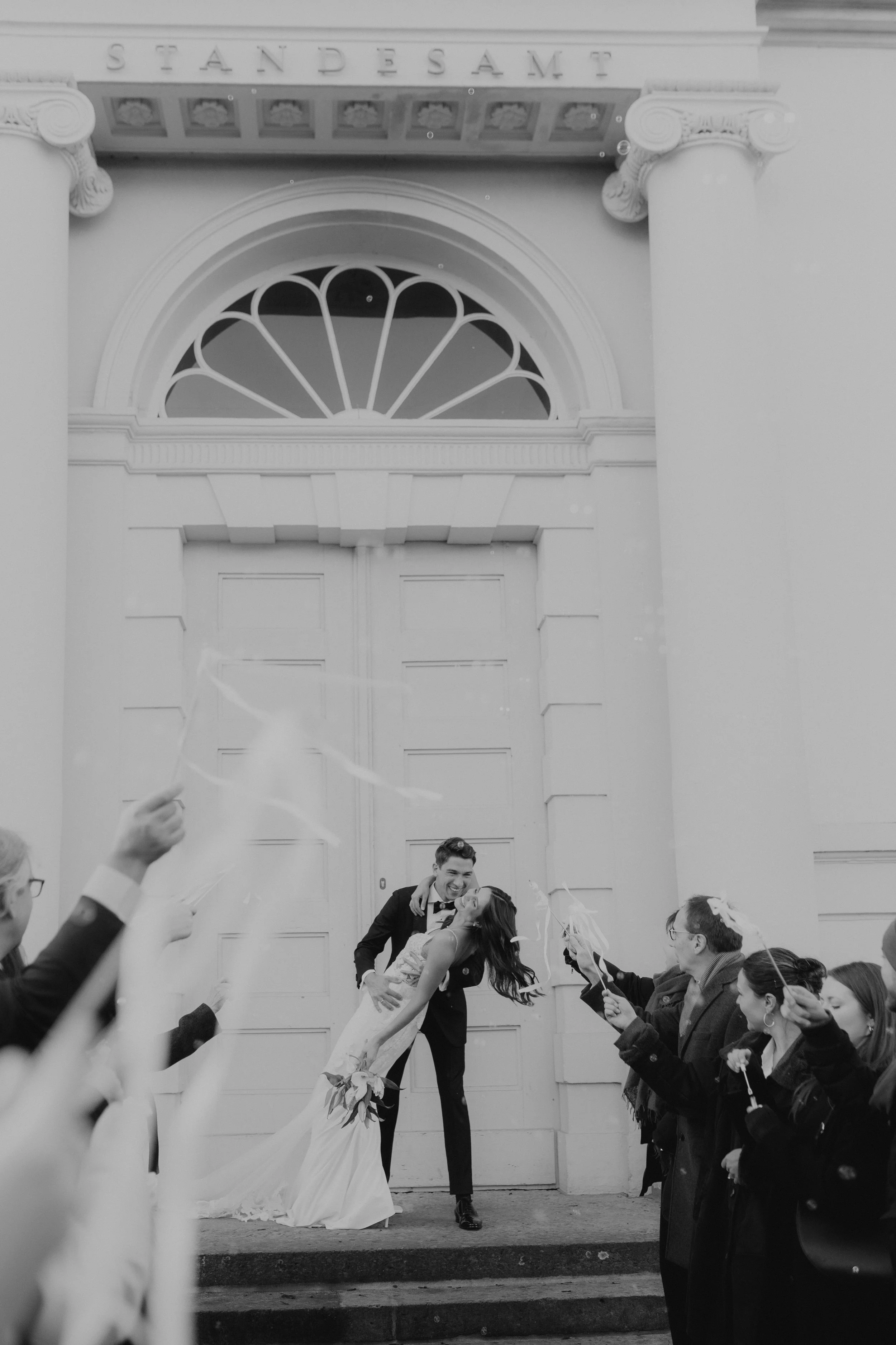 Ein Paar tanzt vor einer weißen Kirche, umgeben von Freunden, die mit konfetti jubeln.