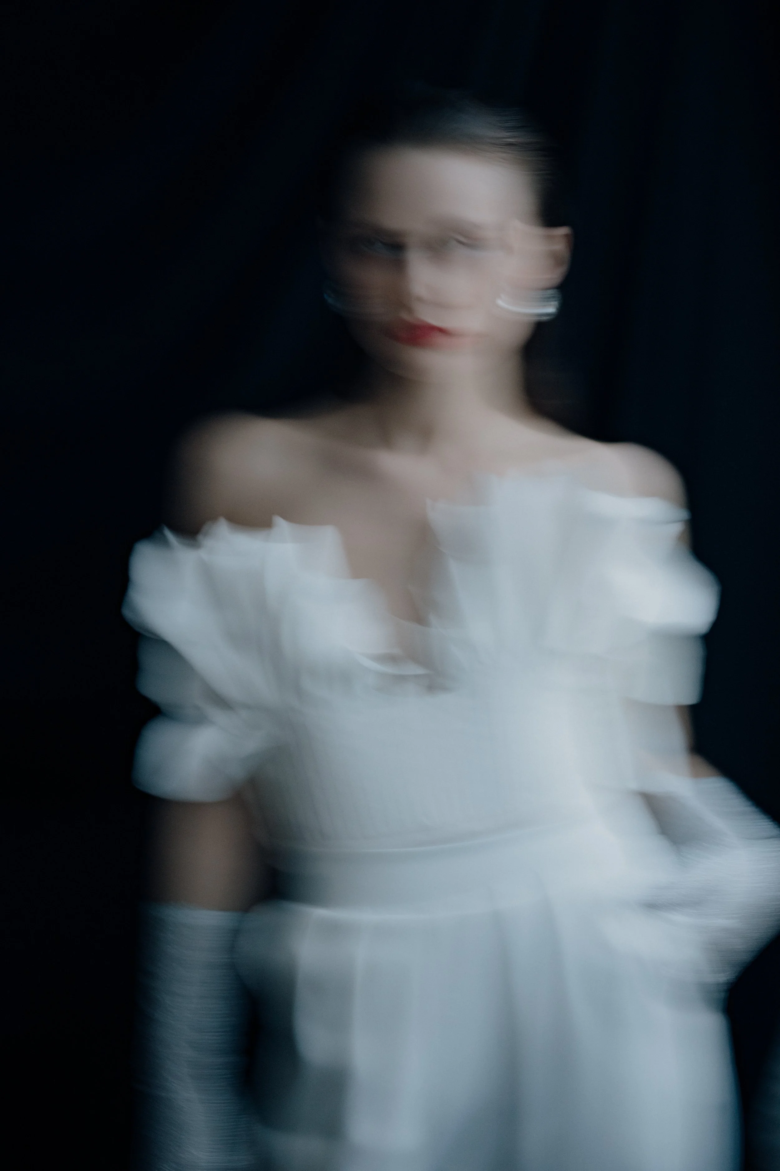 Verwackelte Nahaufnahme einer Frau in einem weißen Kleid vor dunklem Hintergrund.