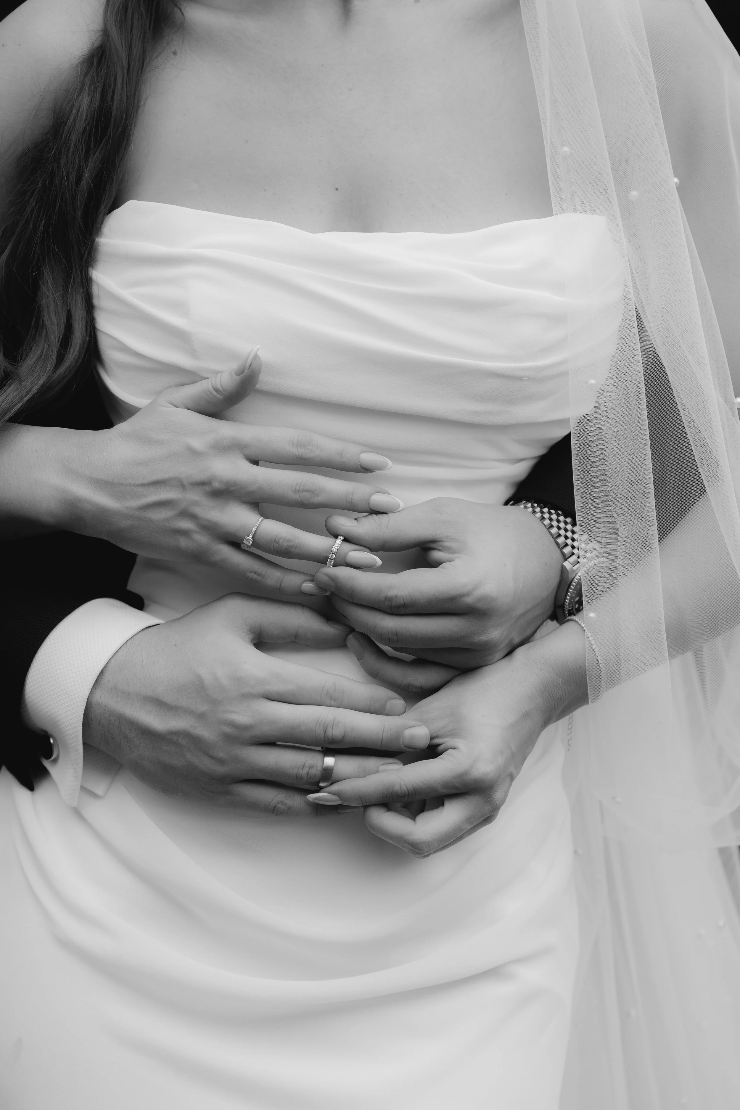 Schwarz-weiß-Foto eines Brautpaares, das sich an den Händen hält und ihre Ringe zeigt, bei ihrer Hochzeit.