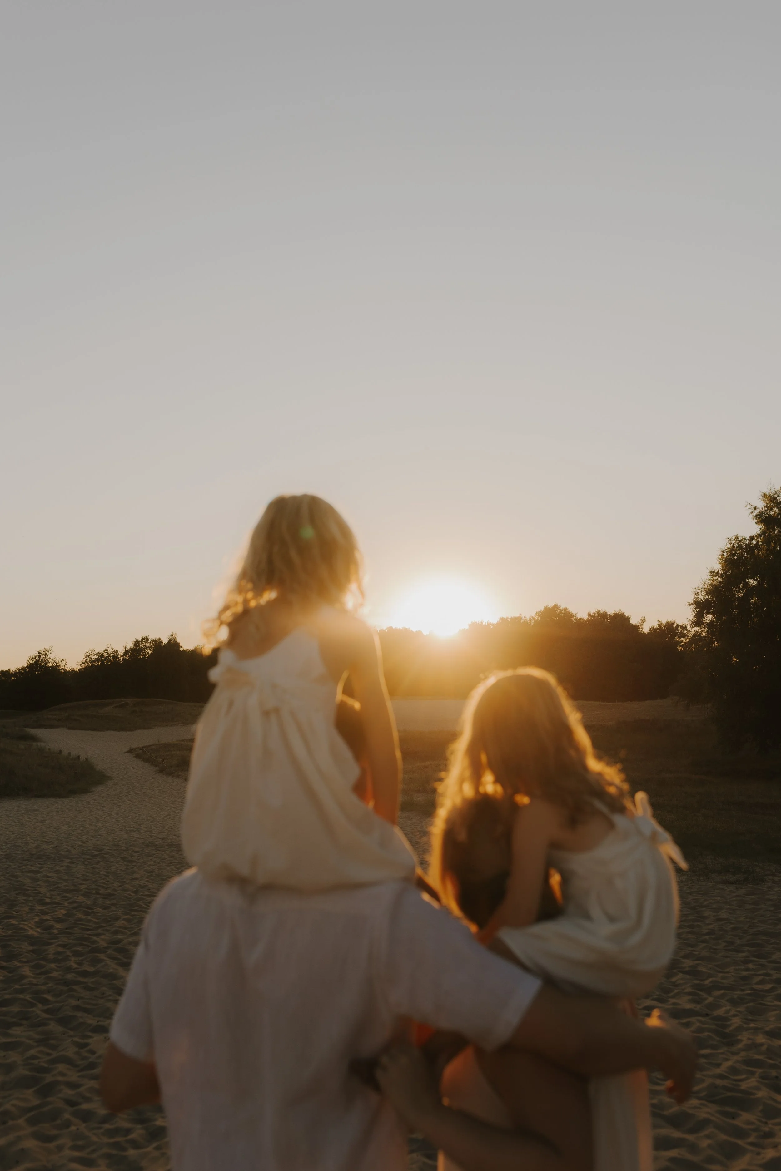 Vater hält zwei kleine Mädchen an einem Strand bei Sonnenuntergang im Sand.