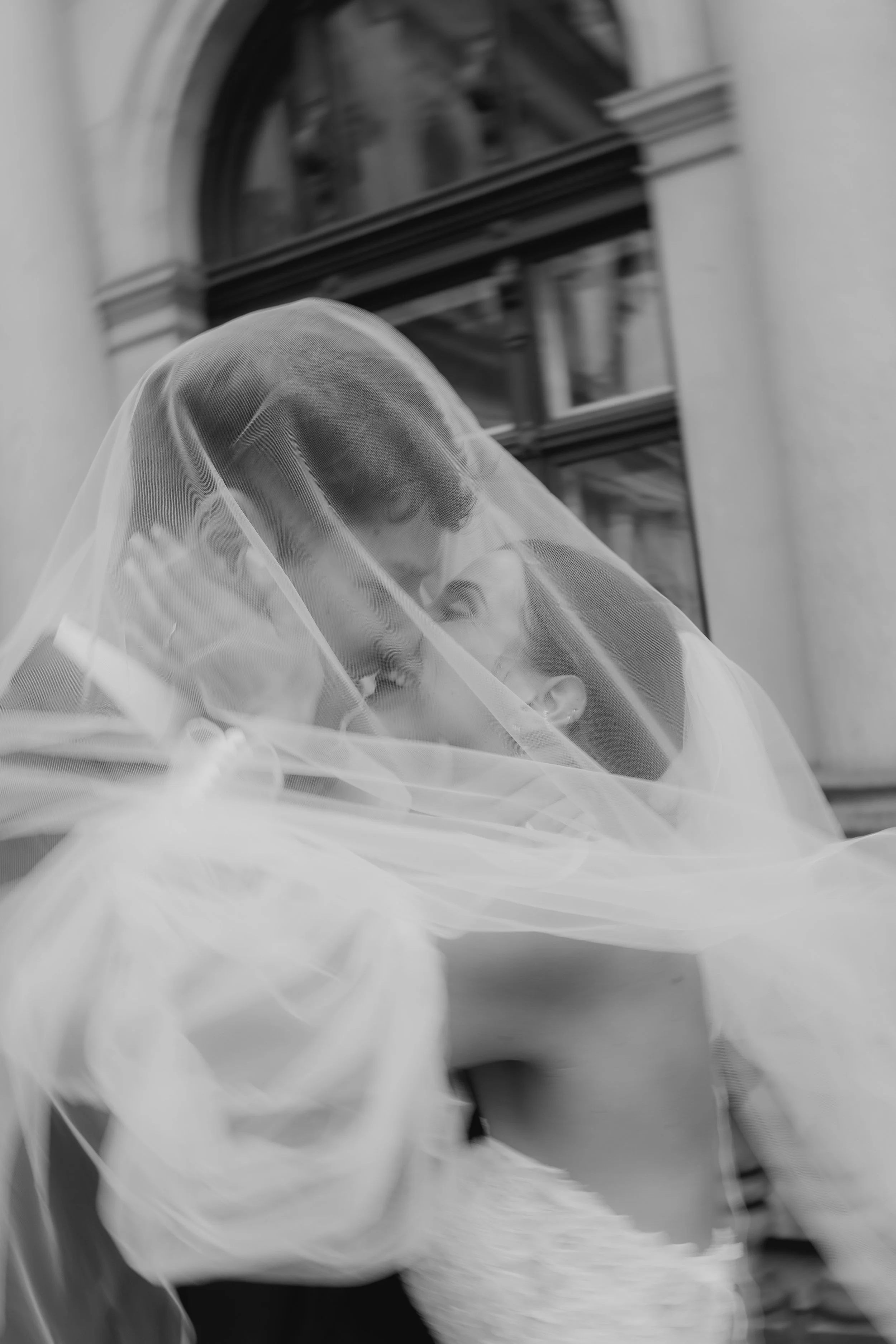 Verliebtes Paar unter einem Tuch, bei einer Hochzeit, in schwarz-weiß fotografiert.