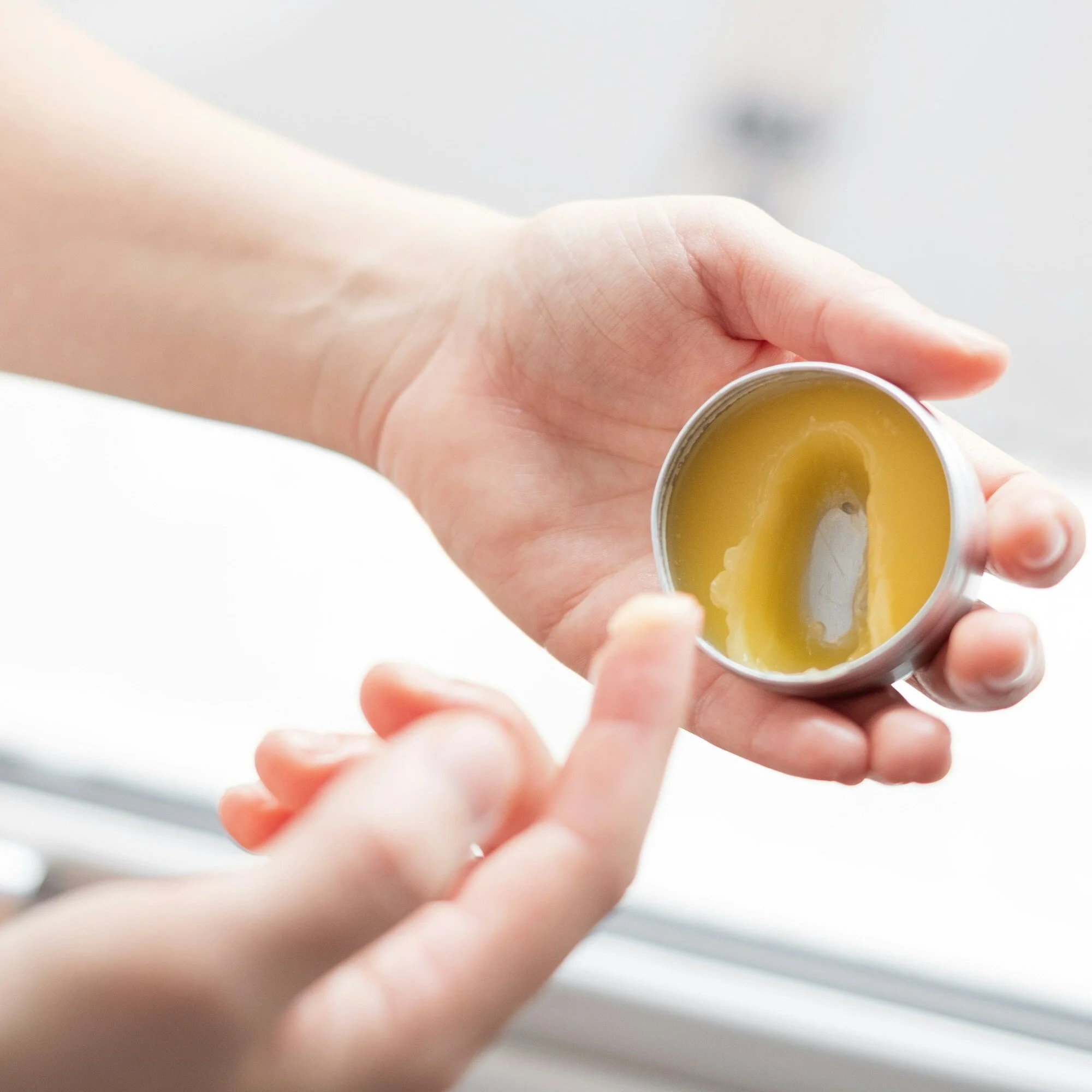 Person holding a small tin of balm, applying it with their finger.
