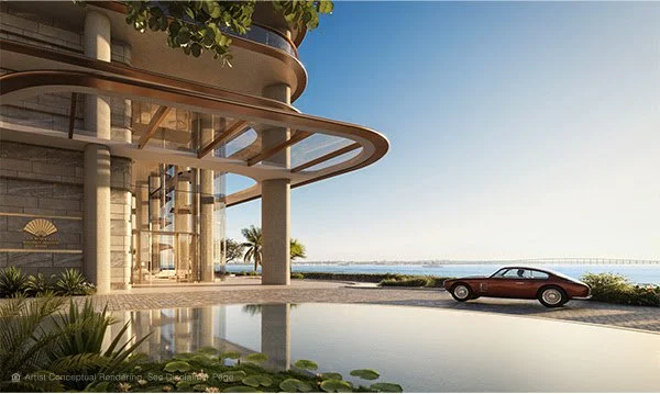 Luxury building entrance with large glass windows, modern architectural design, overlooking a body of water, with a classic car parked near the front and landscaping with lush greenery.