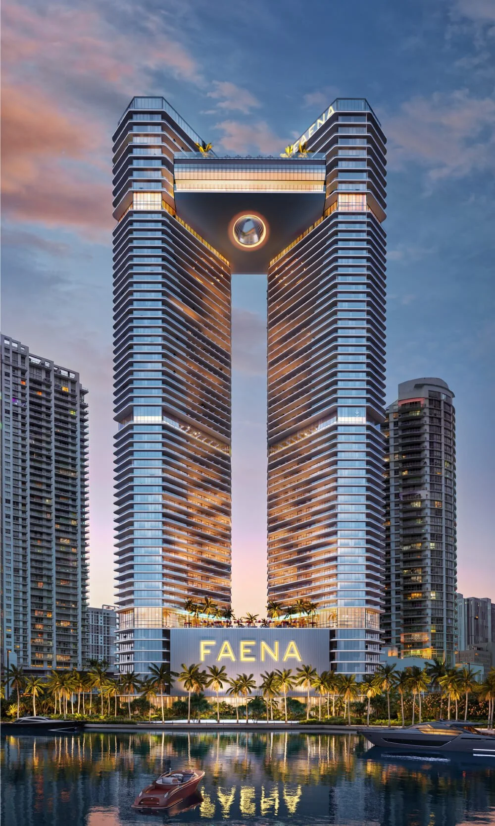 Twin modern skyscrapers of Faena with illuminated logo, palm trees, and yachts on a reflective water surface at dusk.