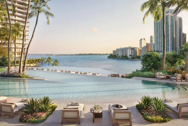 Luxury resort infinity pool overlooking a bay, surrounded by lounge chairs and palm trees, with a city skyline in the background.