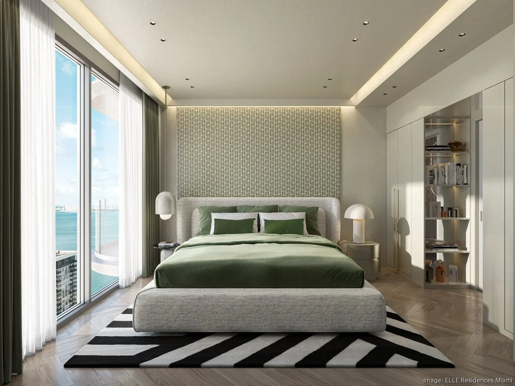 Modern bedroom with large windows, green bedding, patterned rug, geometric accent wall, and built-in shelves.