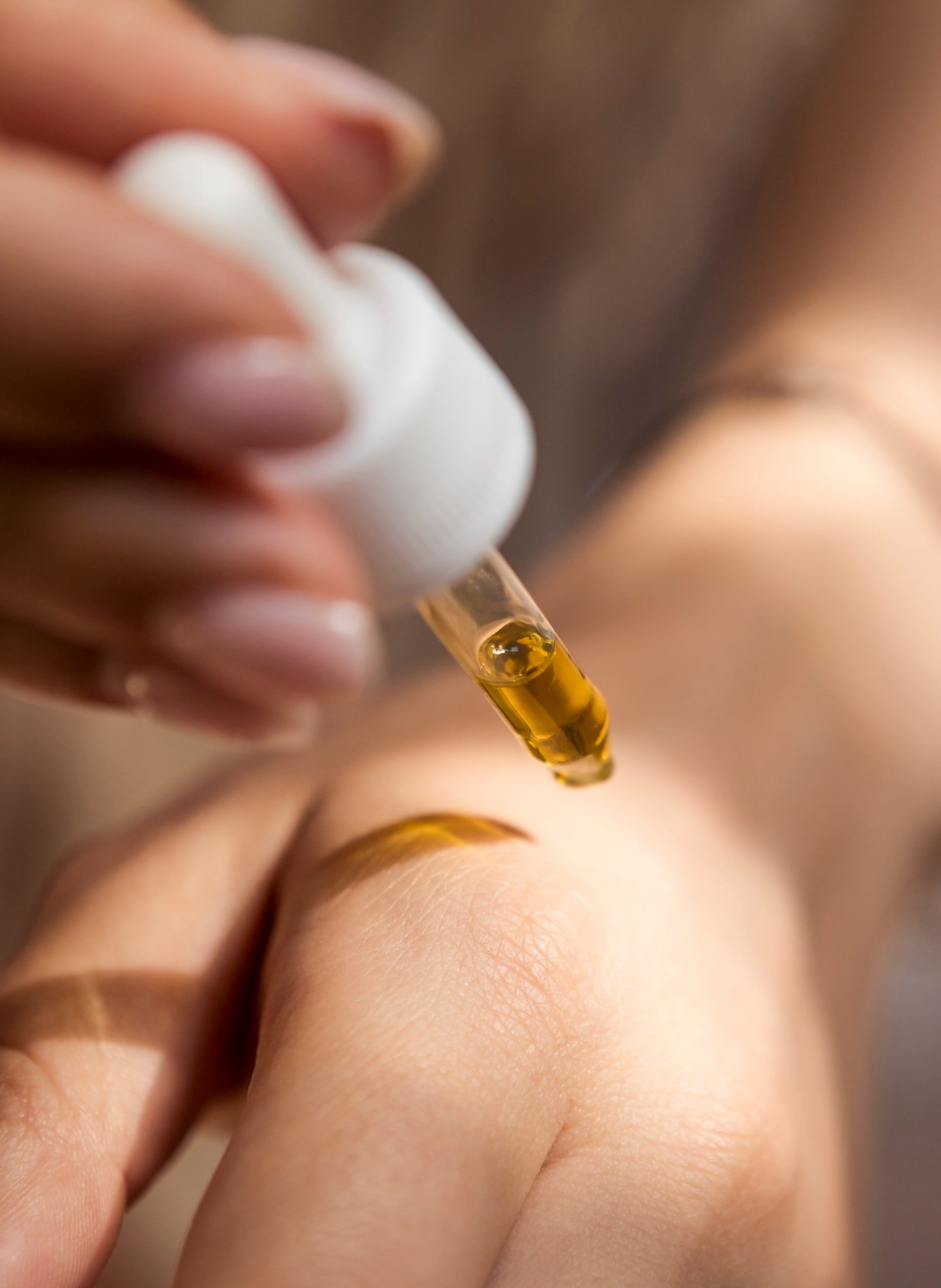 Close-up of a dropper releasing oil onto a person's skin.