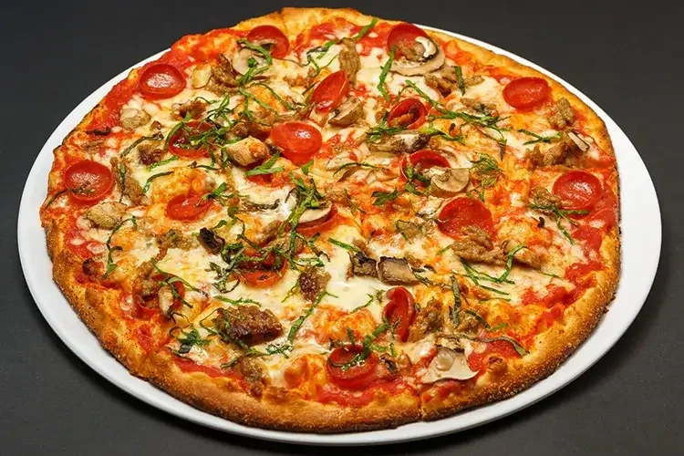 A sliced Pepperoni and Sausage Pizza with green herbs on top served on a white plate against a black background.