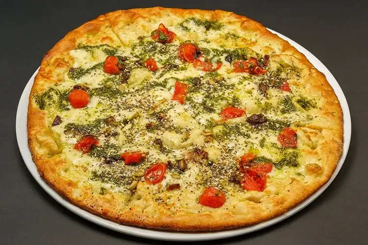 Close-up of a Margherita pizza on a white plate with toppings including cherry tomatoes, cheese, herbs, and seeds, on a black surface