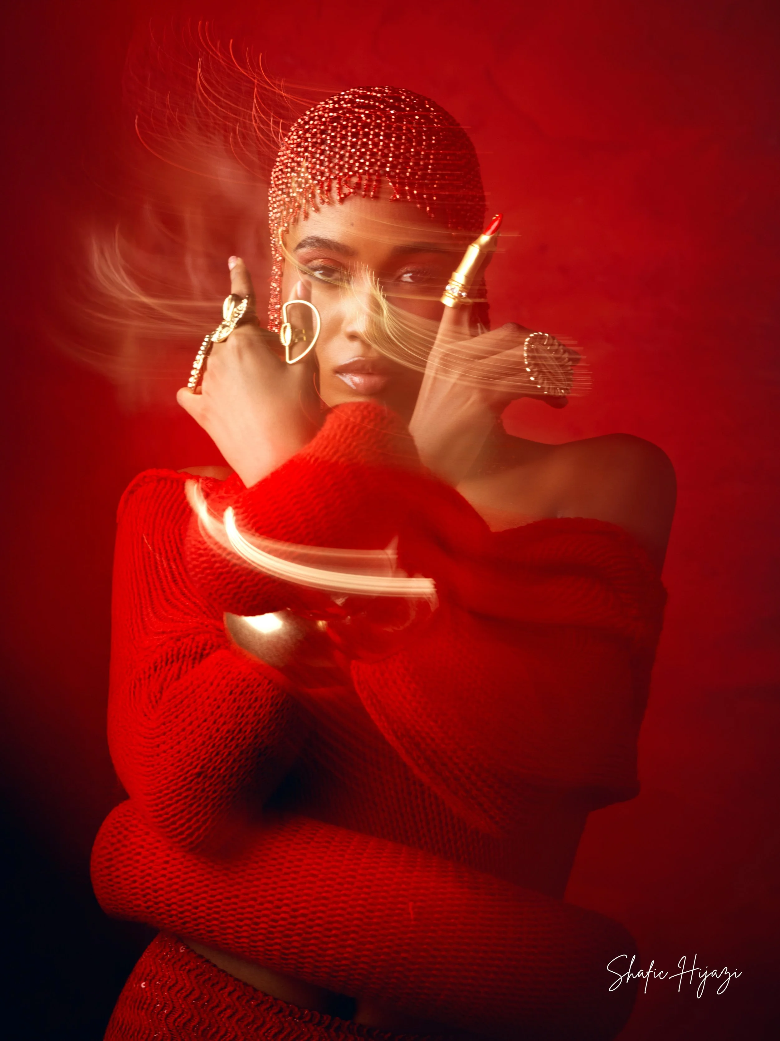 A woman wearing a red knit top and jewelry, with a beaded red headpiece, poses against a red background with motion blur effects.