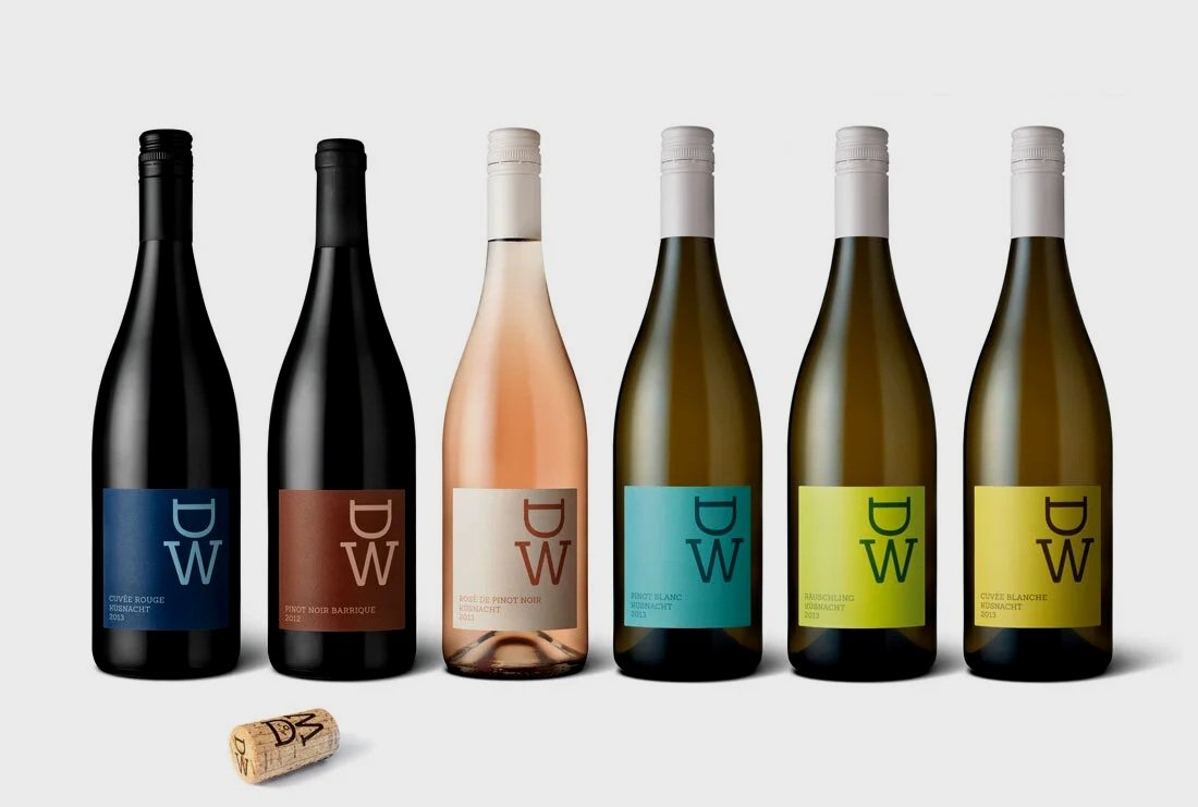 Nahaufnahme einer Person, die eine Flasche Wein hält, mit dunklem Etikett, auf dem 'D W' und 'Cuvée Rouge Kusnacht 2013' steht.