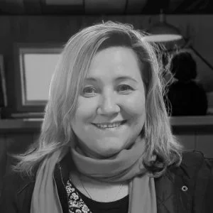 Black and white photo of a smiling woman with shoulder-length hair, wearing a scarf and a jacket.