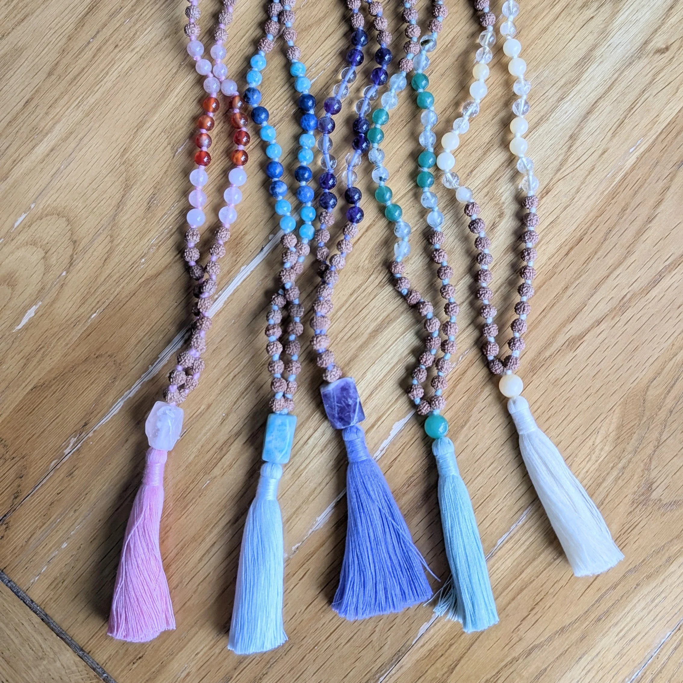 A collection of beaded necklaces with tassels in various pastel colors, laid out on a wooden surface.