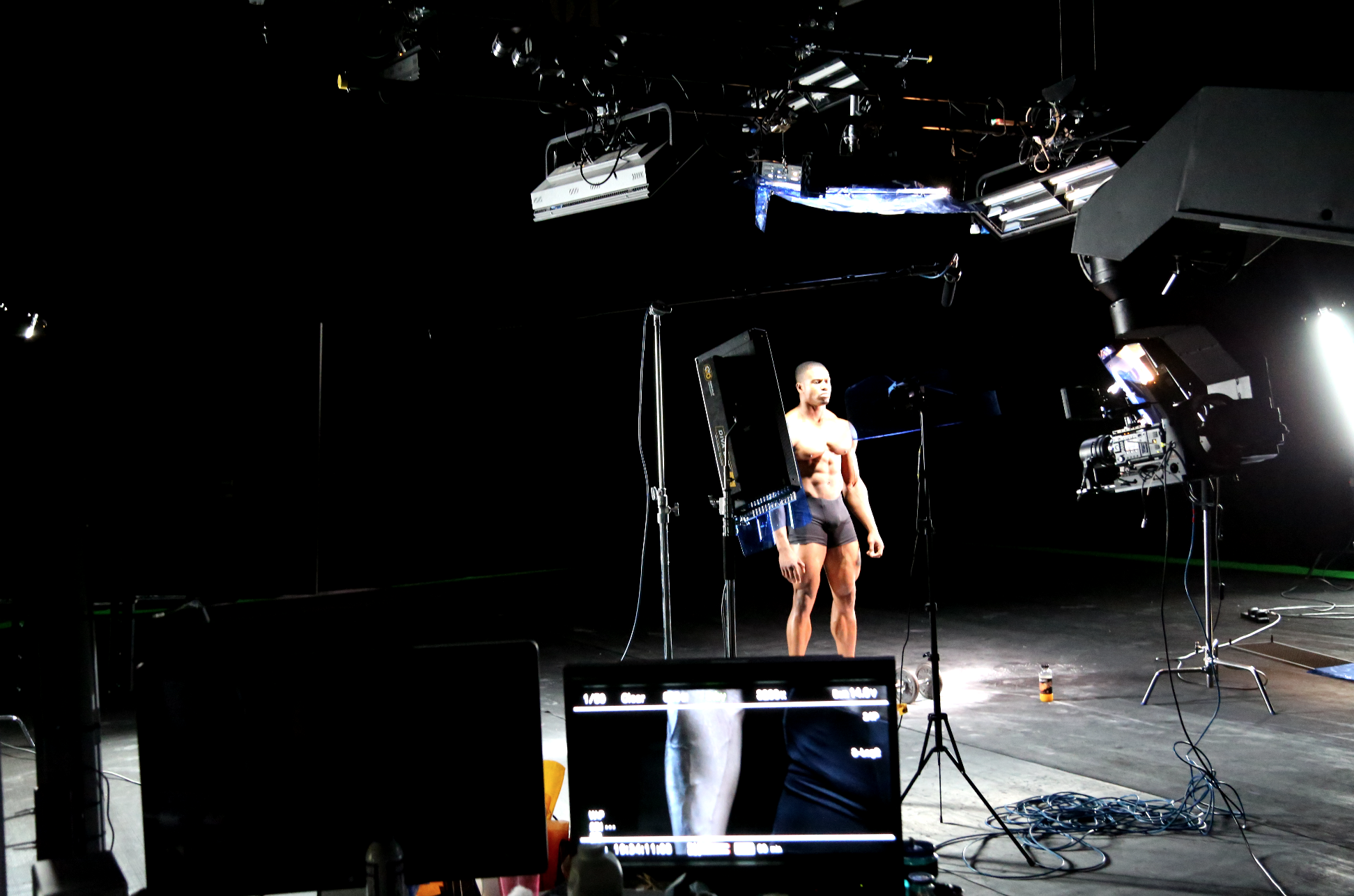 Studio setup with lights and equipment, featuring a man in shorts standing under bright lights, against a dark background.