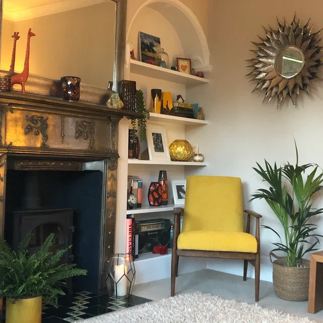 A cozy living room corner with a fireplace, decorative objects, and a yellow vintage mid-century armchair.