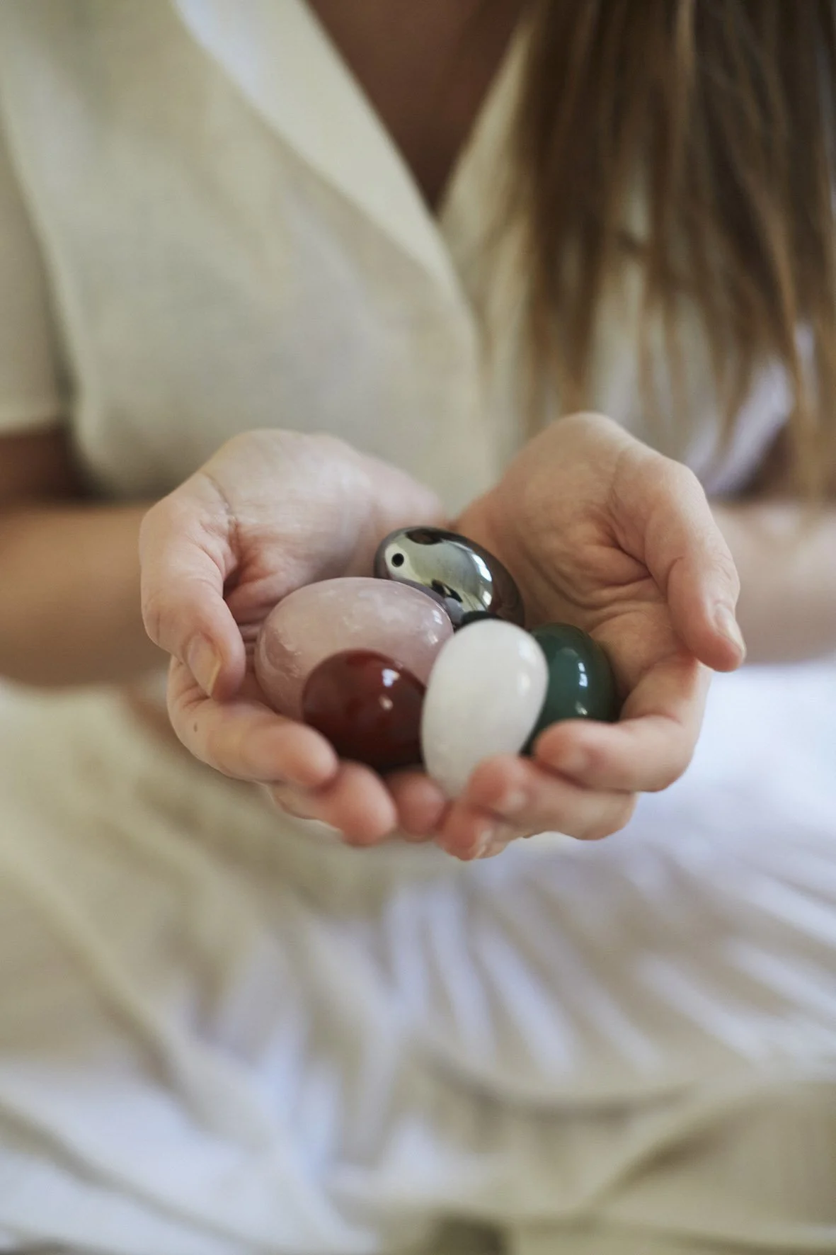 A person holding several polished stones of various colors and sizes.