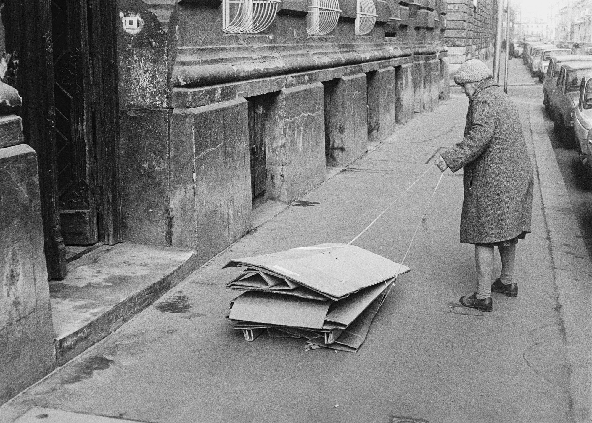 Photo noir et blanc de Hans van der Meer montrant une vieille dame tirant un empilement de cartons pliés avec une ficelle, sur un trottoir.