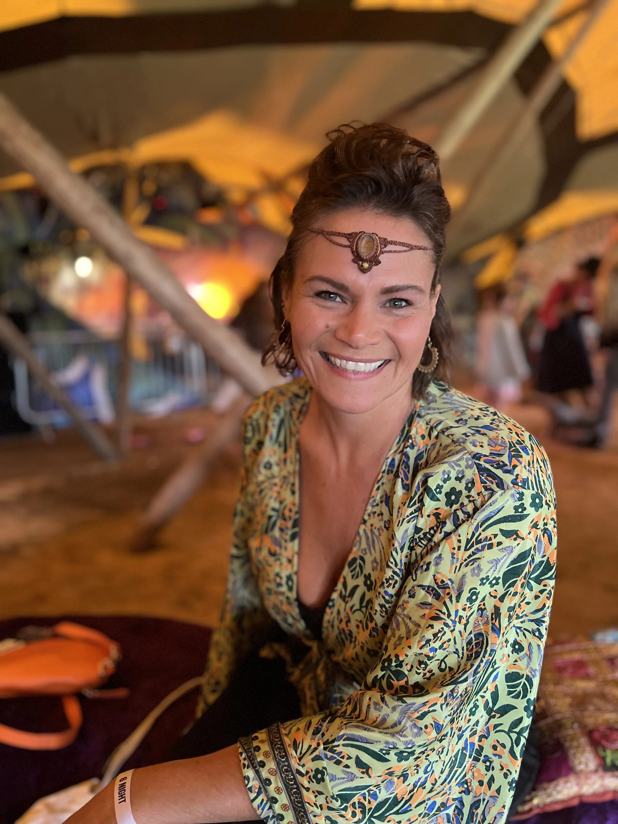 Smiling person wearing a patterned shirt and decorative headpiece at an indoor event.