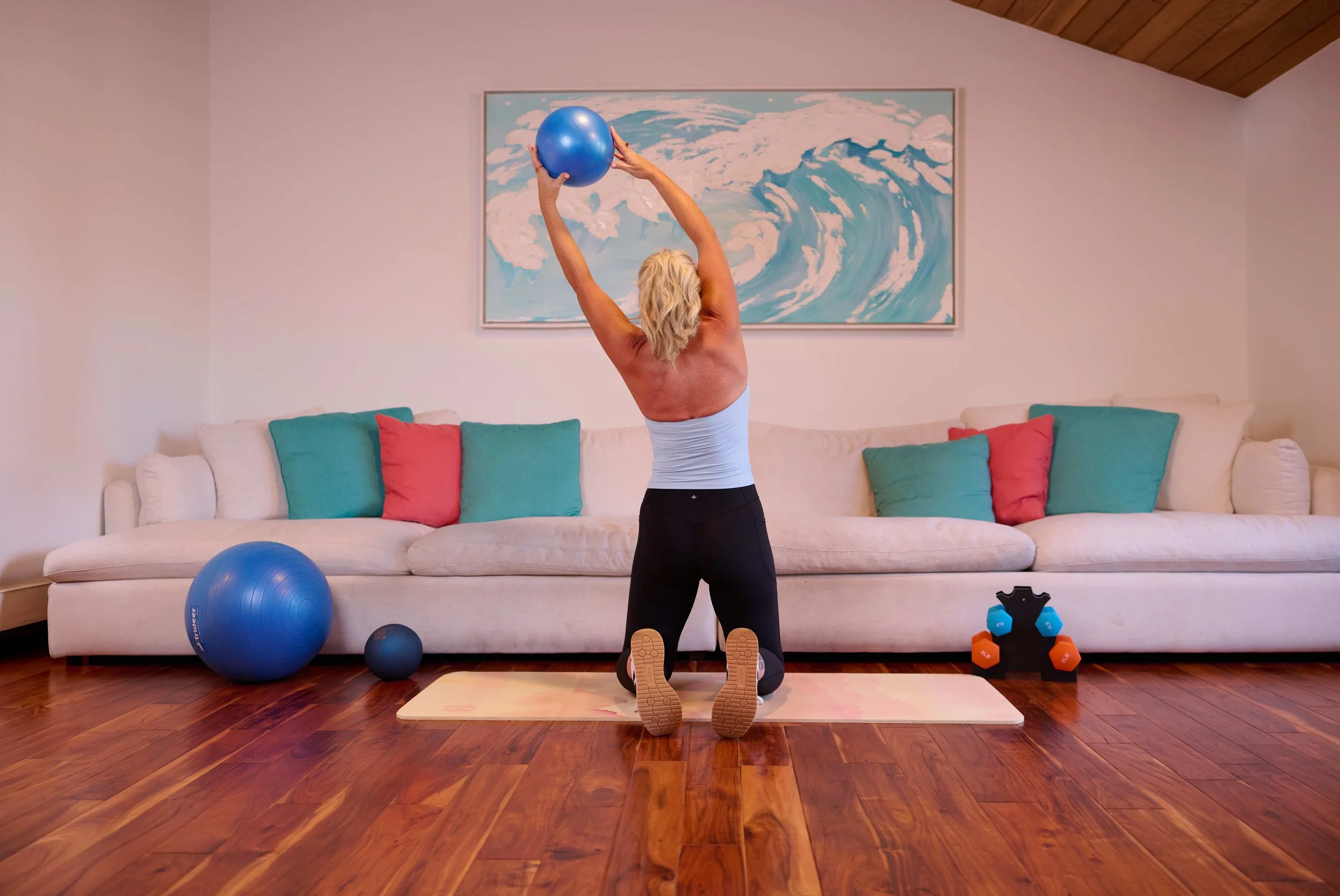 woman doing a left side stretch with a medicine ball in her hands in front of a cream couch