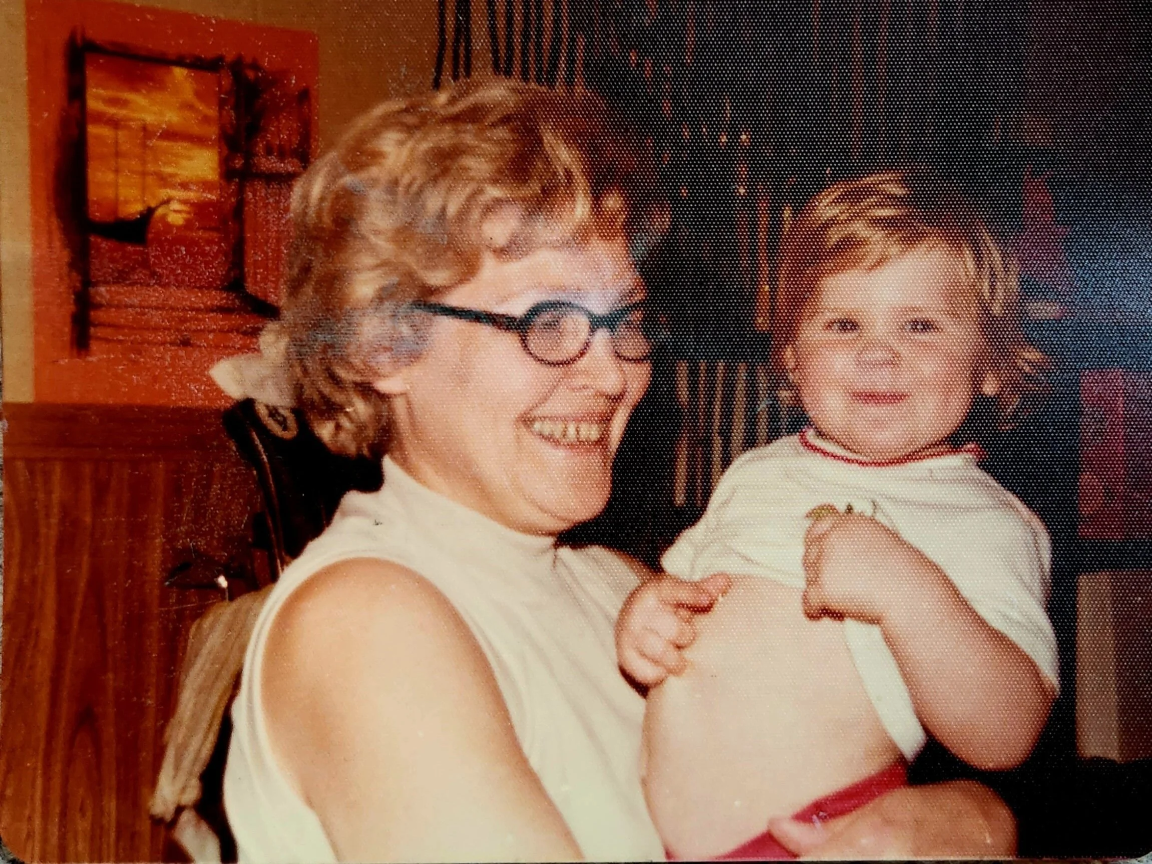 a little girl around 2 years old held by her grandmother in glasses and smiling
