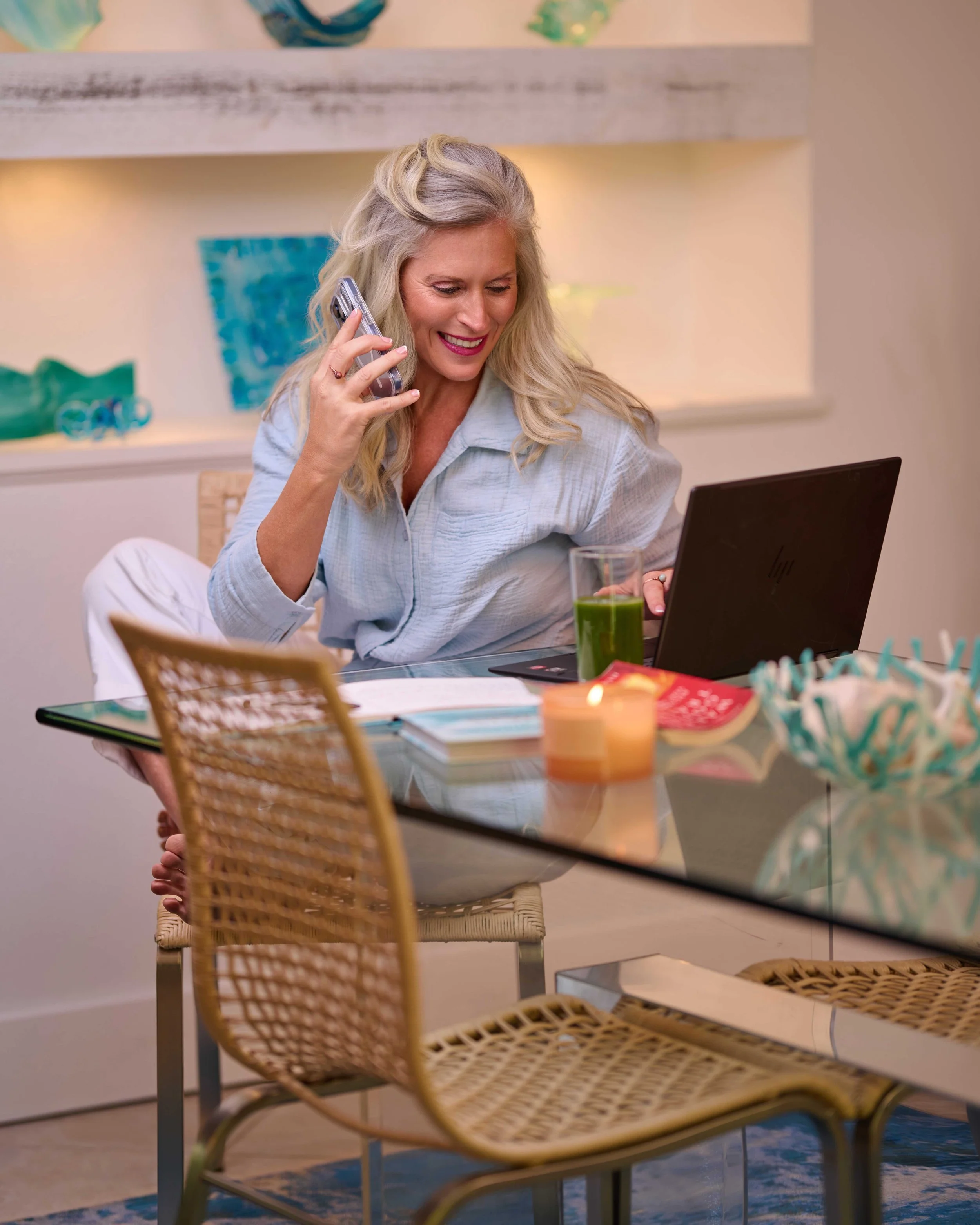 woman sitting down holding a phone up to her hear while smiling at her laptop