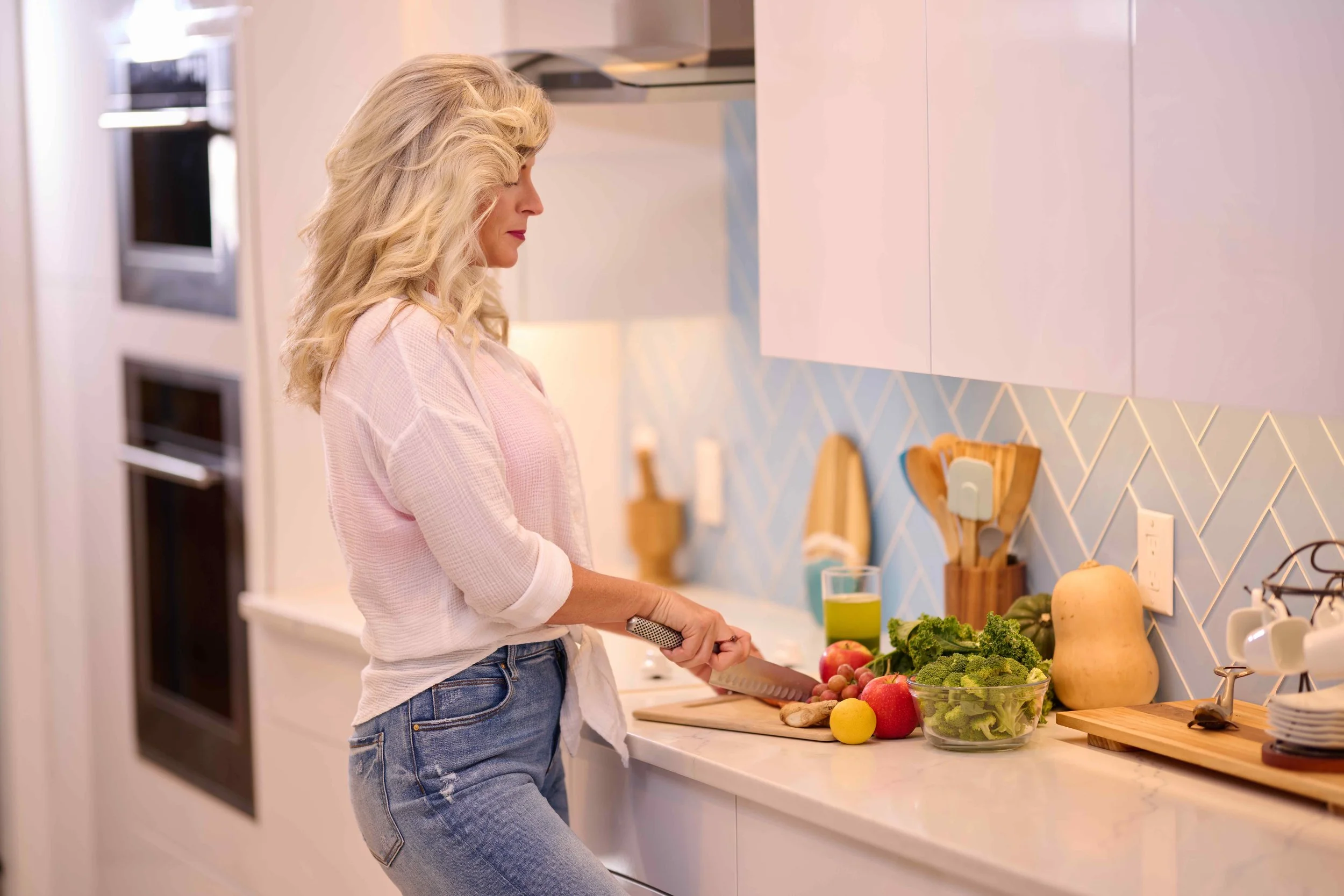 a woman in a white shirt and jeans chopping vegetables in a white and blue kitchen