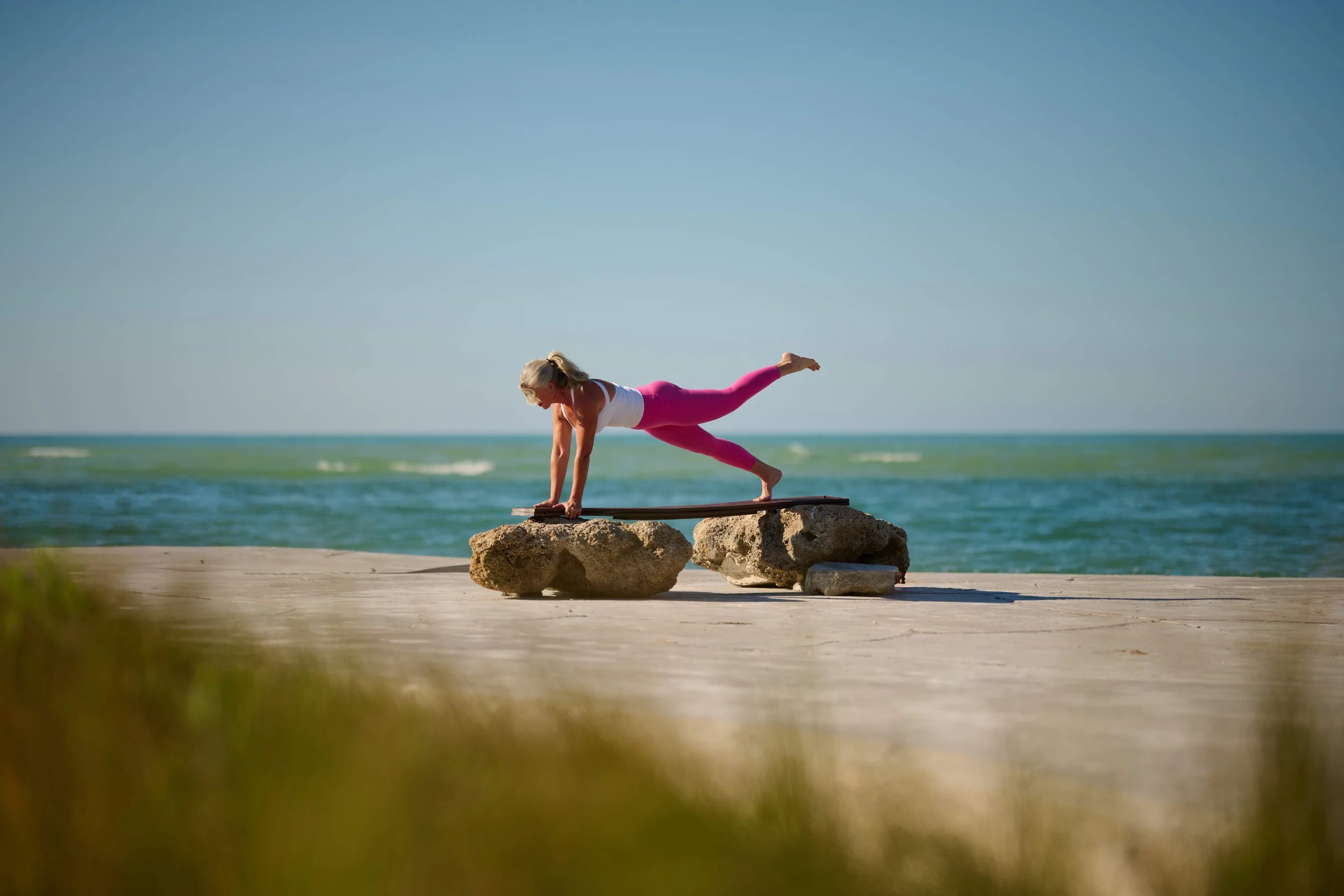 women balancing on a bench in front of the ocean