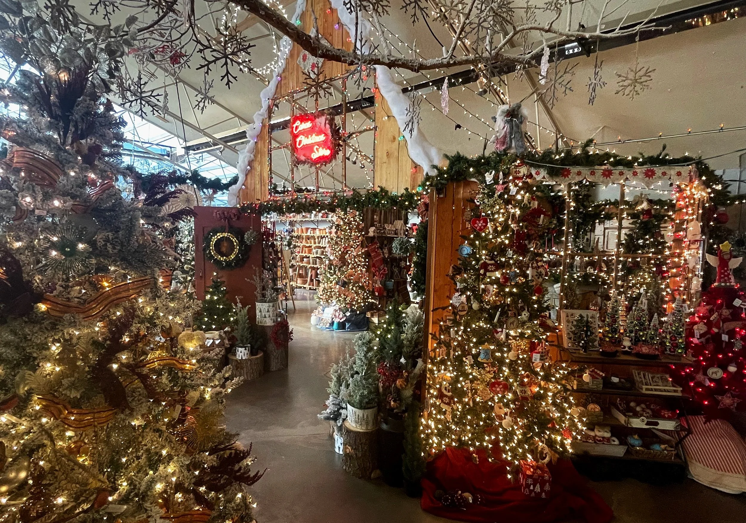 A festive holiday store scene decorated with Christmas trees, lights, garlands, ornaments, and snowflake ornaments hanging from the ceiling.