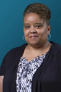 Smiling person wearing black cardigan and patterned blouse against blue background