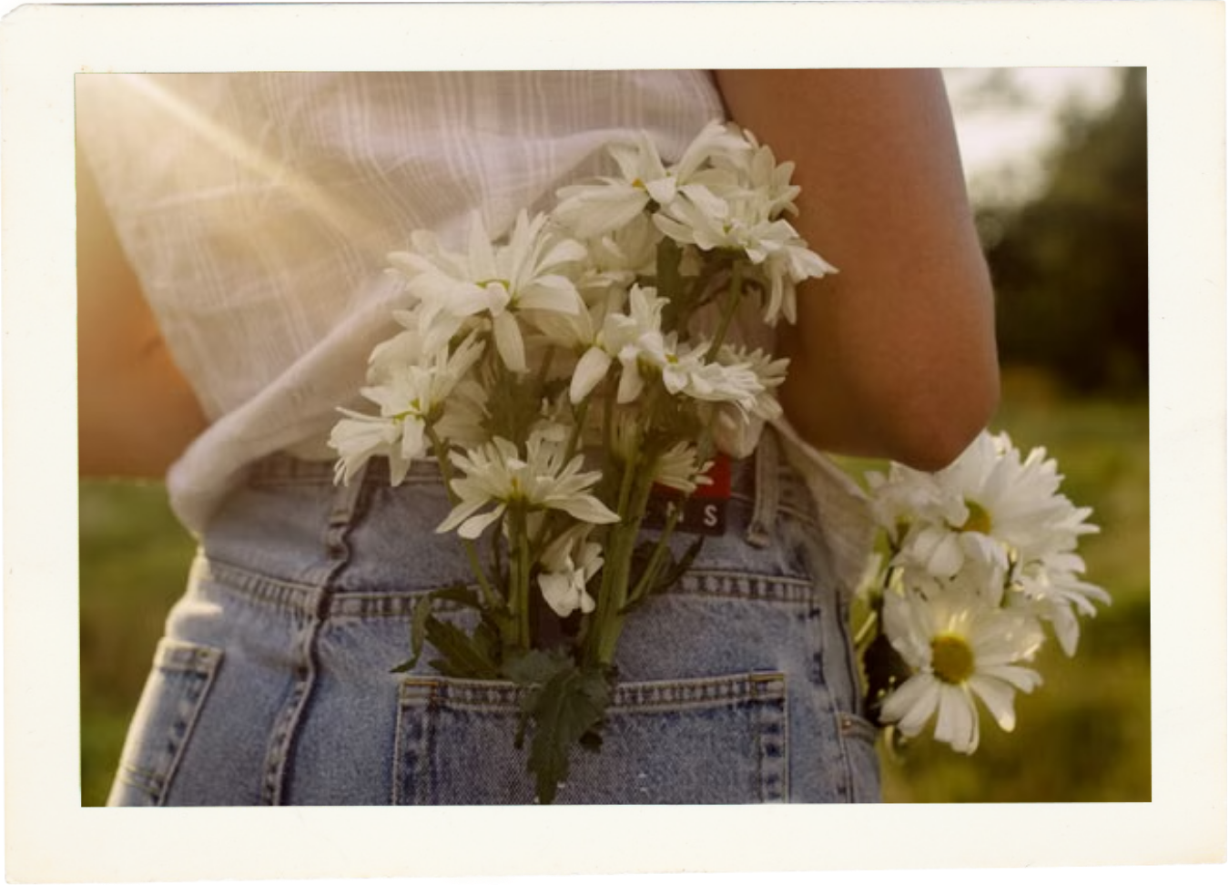 Woman holding white flowers tucked behind her back pocket.