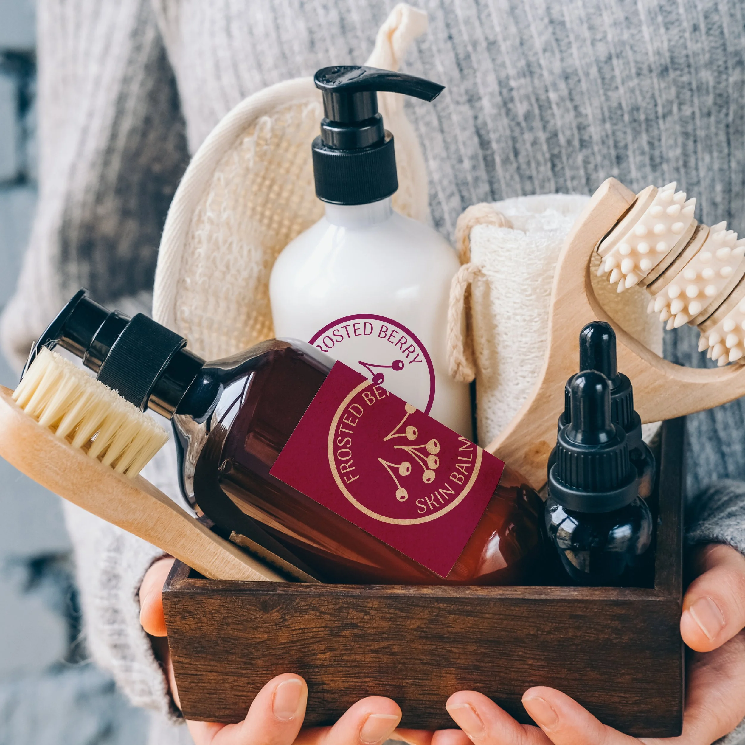 A wooden tray holding various skincare products, including a white pump bottle, a brown bottle with a black lid, and a bamboo facial brush, with a person holding the tray.