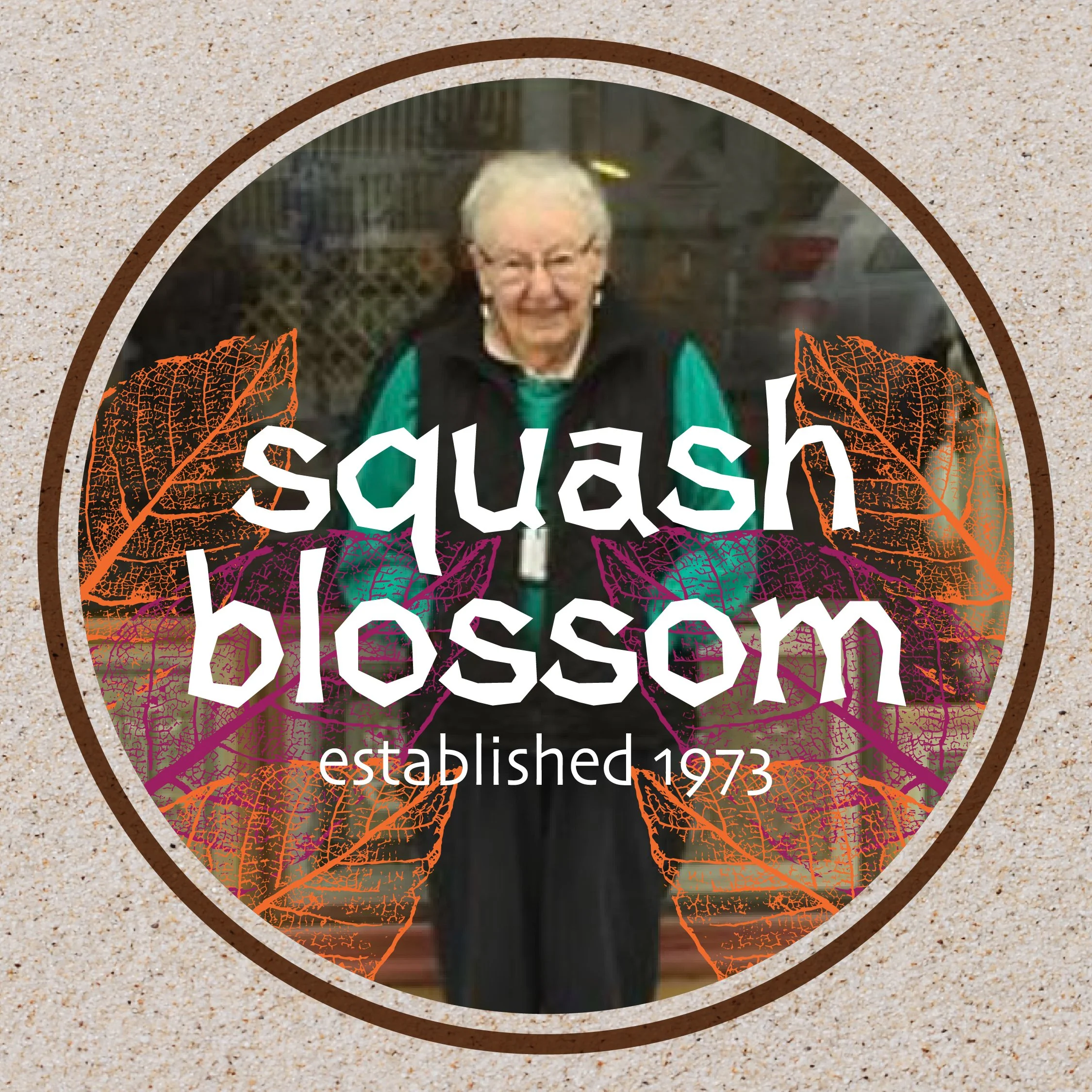 A person smiling outdoors, with blurred greenery in the background, on a circular sticker with autumn leaves and text, on a sandy surface.
