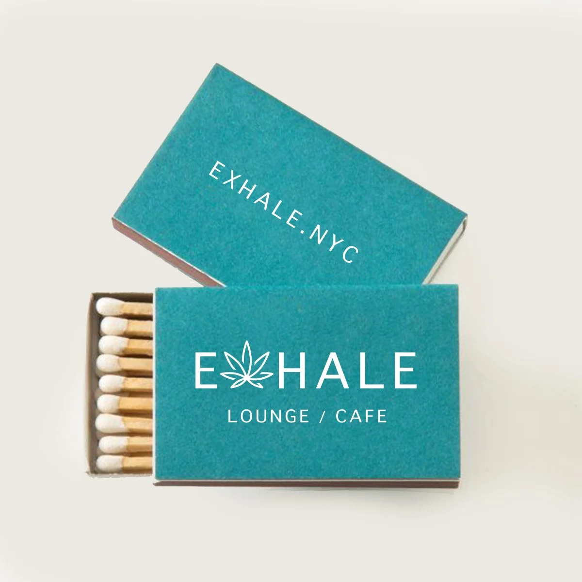 A box of matches with a teal cover that reads 'EHALE Lounge / Cafe' and a leaf logo, placed next to an open box with similar teal cover and the words 'Exhale: NYC'.