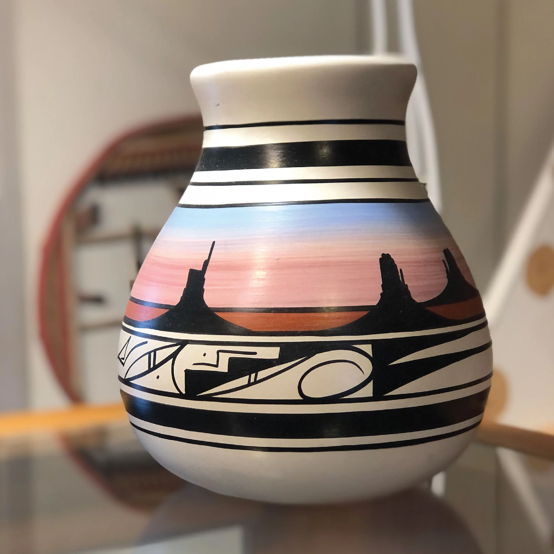 Close-up of a white ceramic mug with black horizontal stripes and black silhouette of a city skyline, seen from below and slightly out of focus.