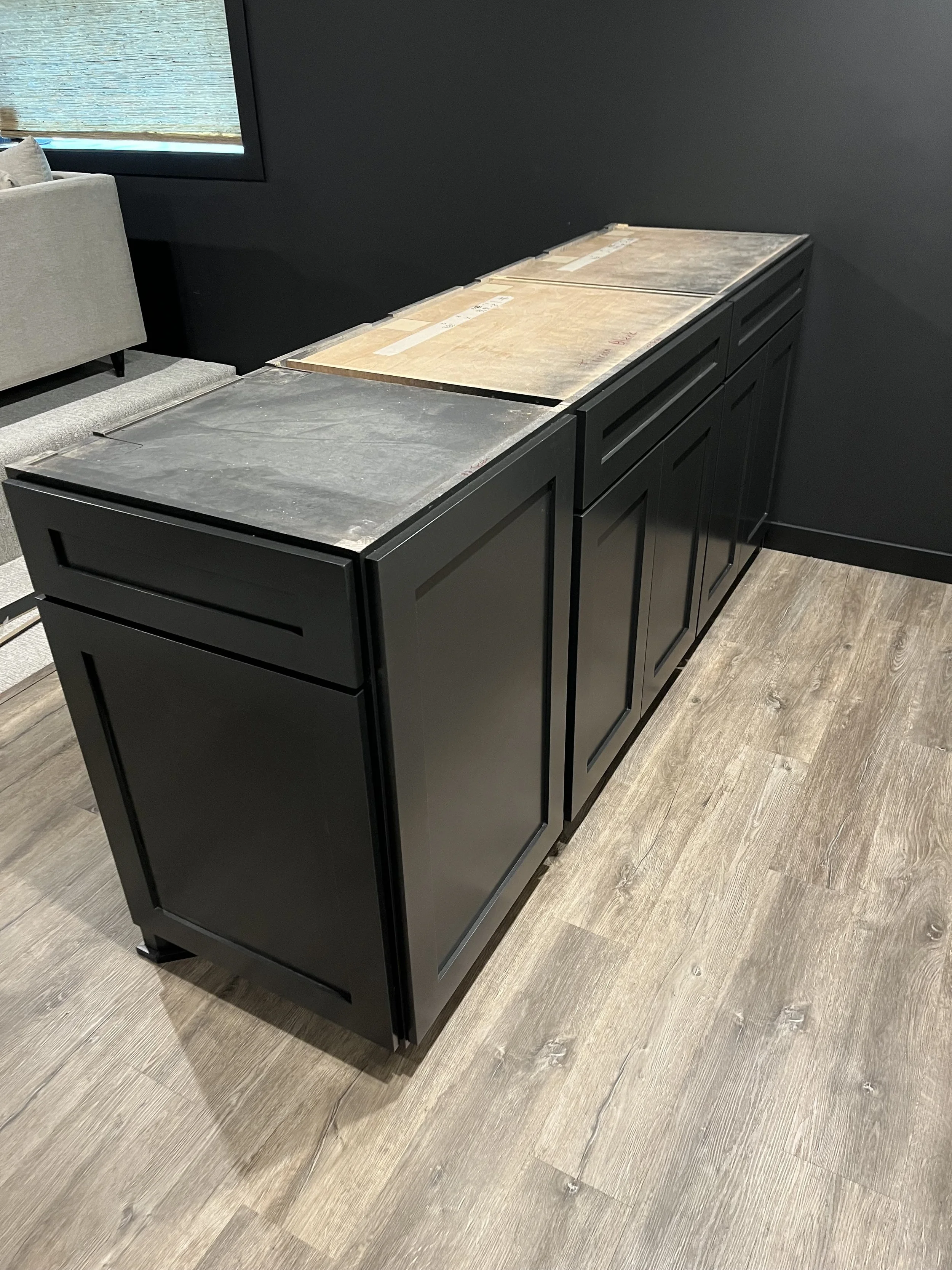Black kitchen cabinets without countertops on a wooden floor.