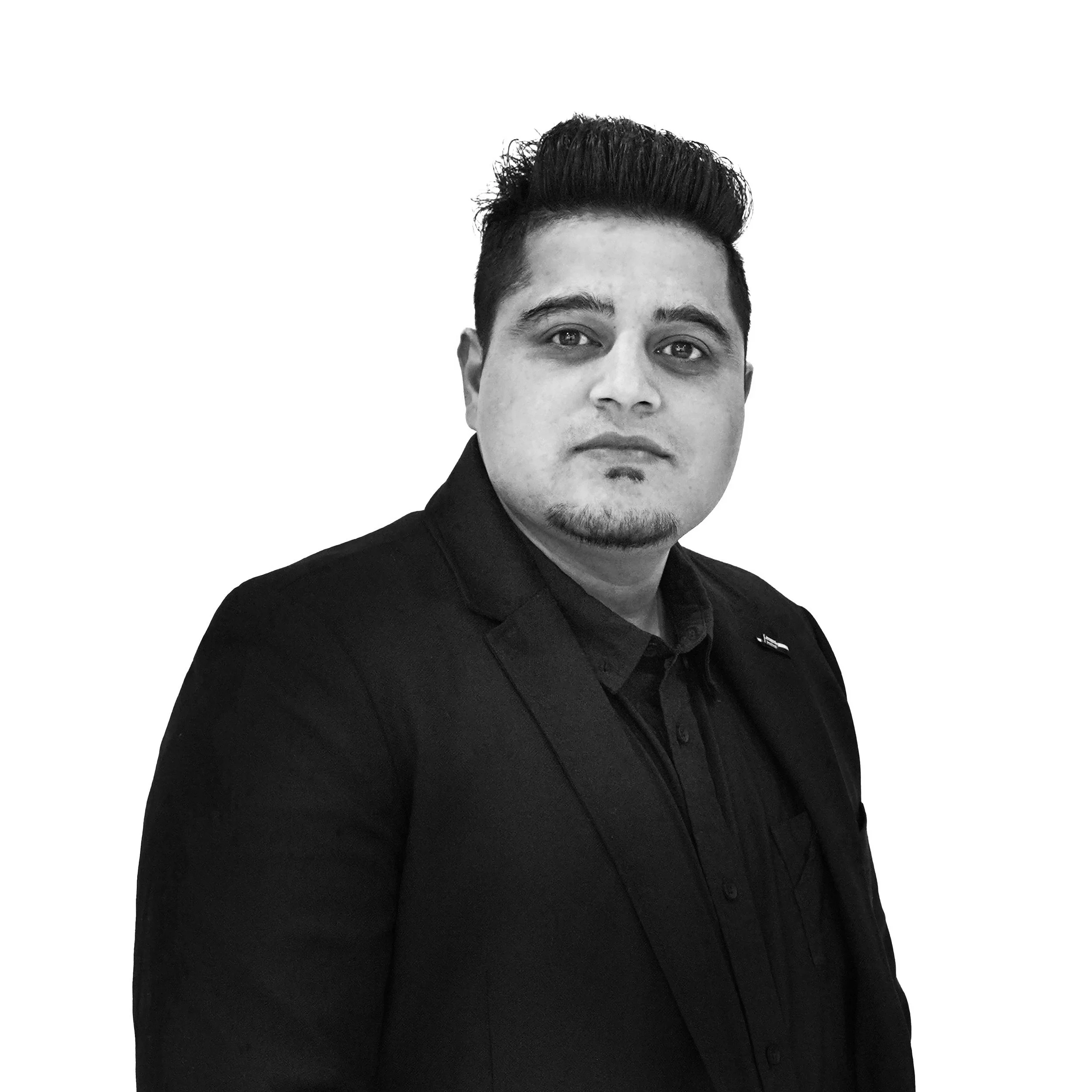 Black and white portrait of a man with styled hair and a goatee, wearing a black blazer and shirt, against a plain white background.