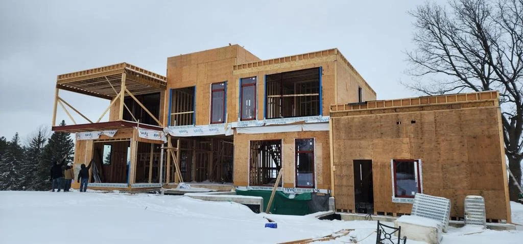 Construction site of a two-story house in winter with wooden framing and workers present.