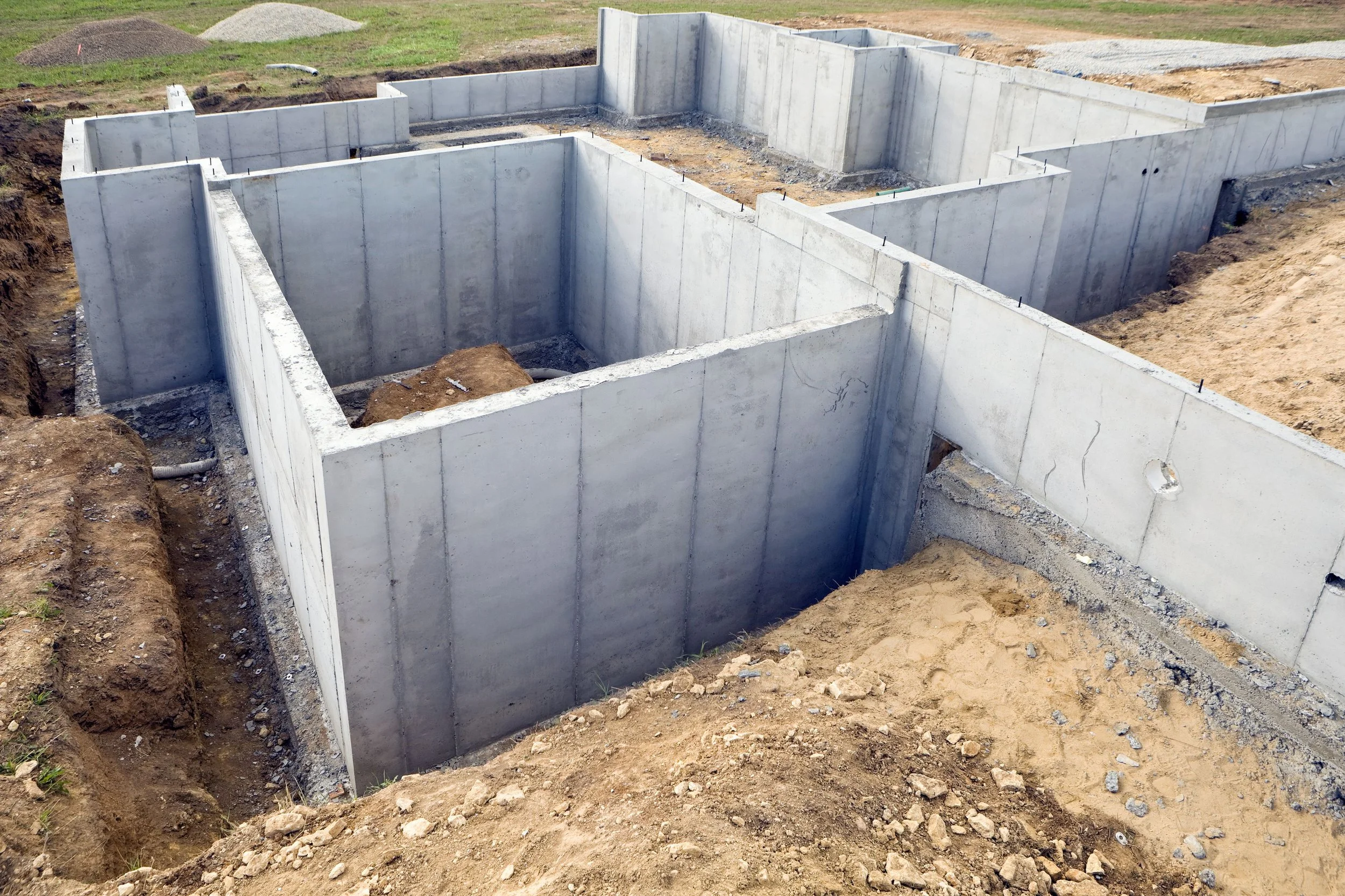 Concrete foundation walls for a building under construction, with exposed dirt and gravel around the site.