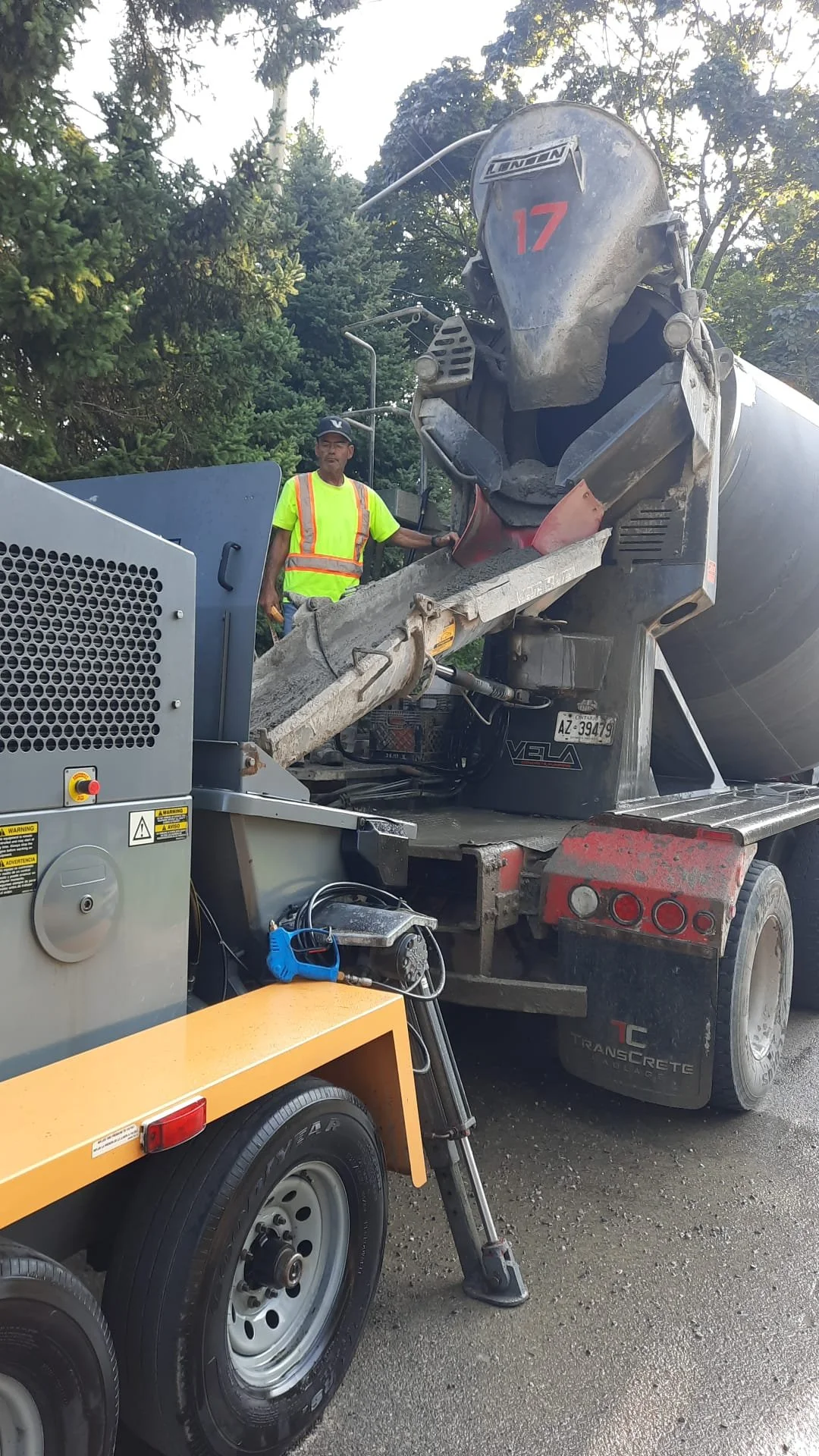 Construction worker operating concrete mixer truck on a road with trees in the background.