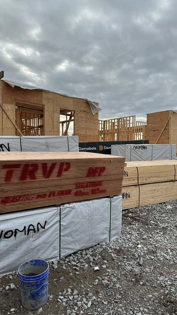 Construction site with wooden framing, stacked lumber, and a cloudy sky.
