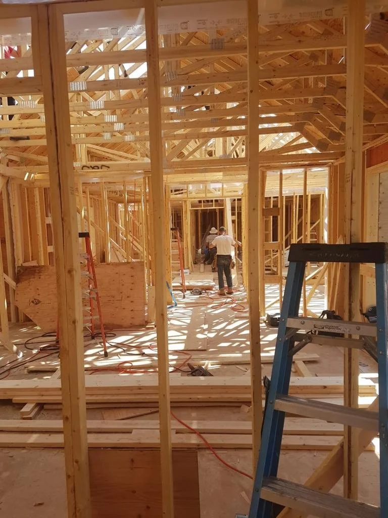 Interior view of a house under construction with wooden framing, ladders, and workers installing the structure.
