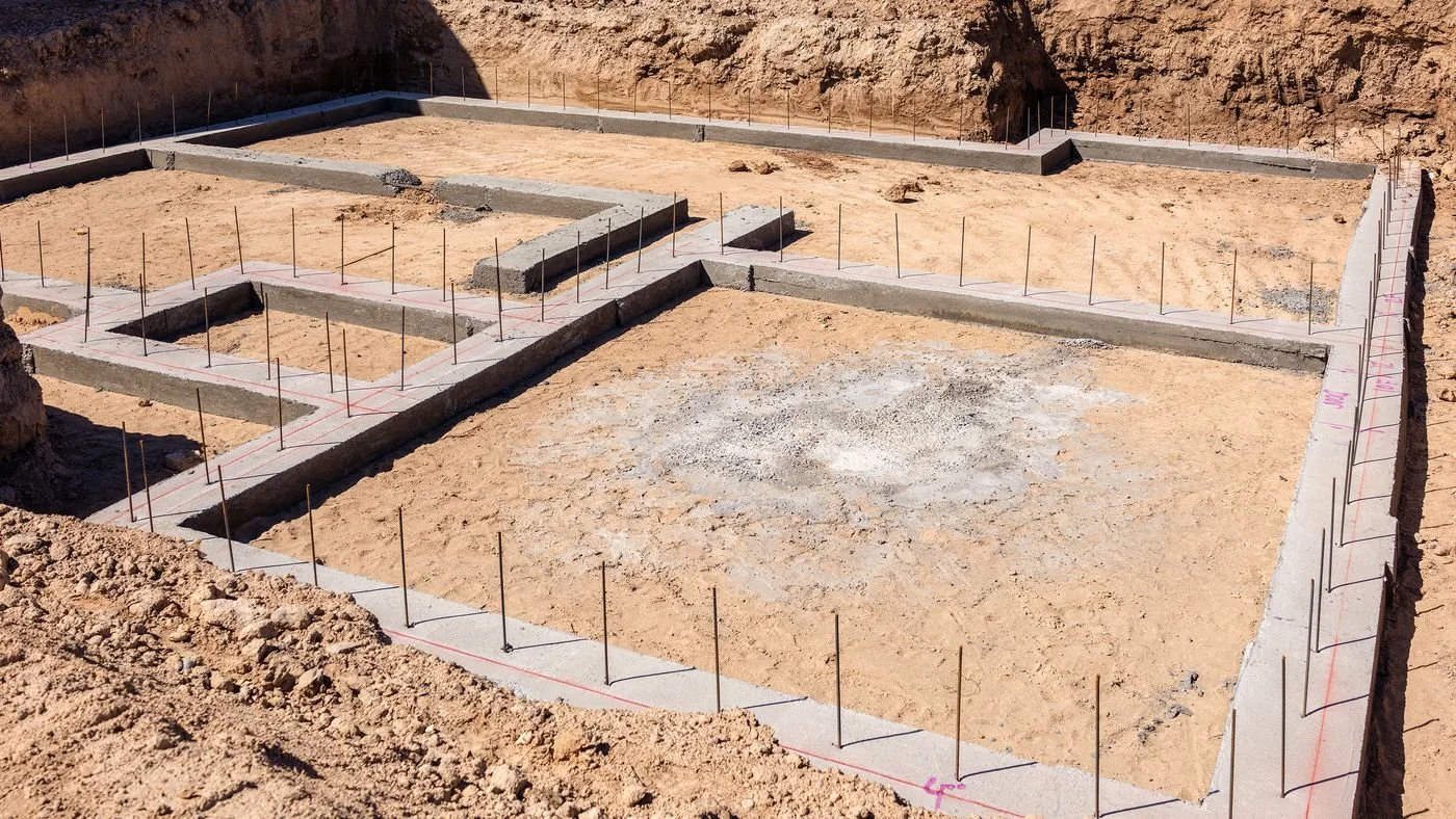 Construction site with concrete foundation outlines and rebars in an excavated area.