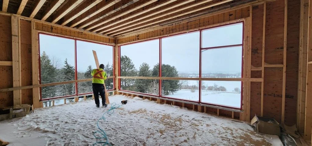 Construction worker in a partially built structure with large window openings and snow outside.