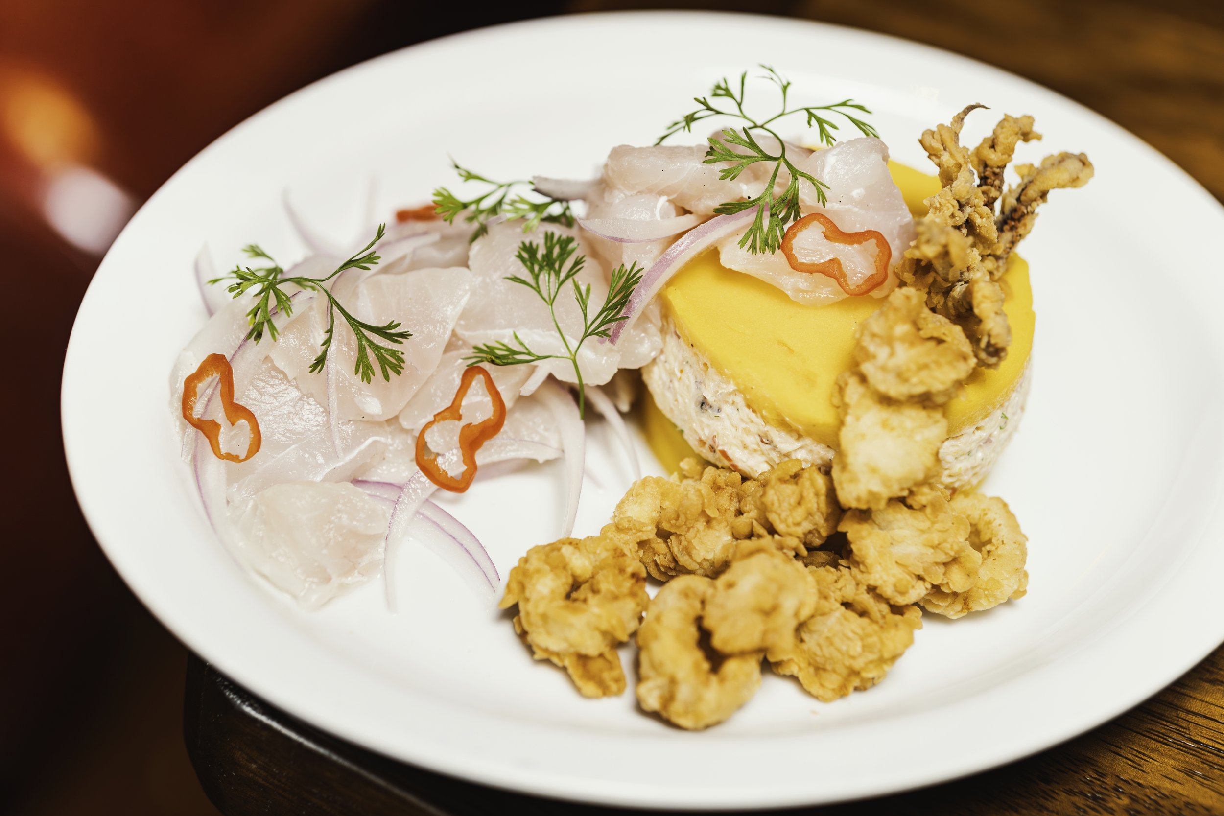 Plato de pescado con ensalada y puré de papa, decorado con hierbas y pimientos.