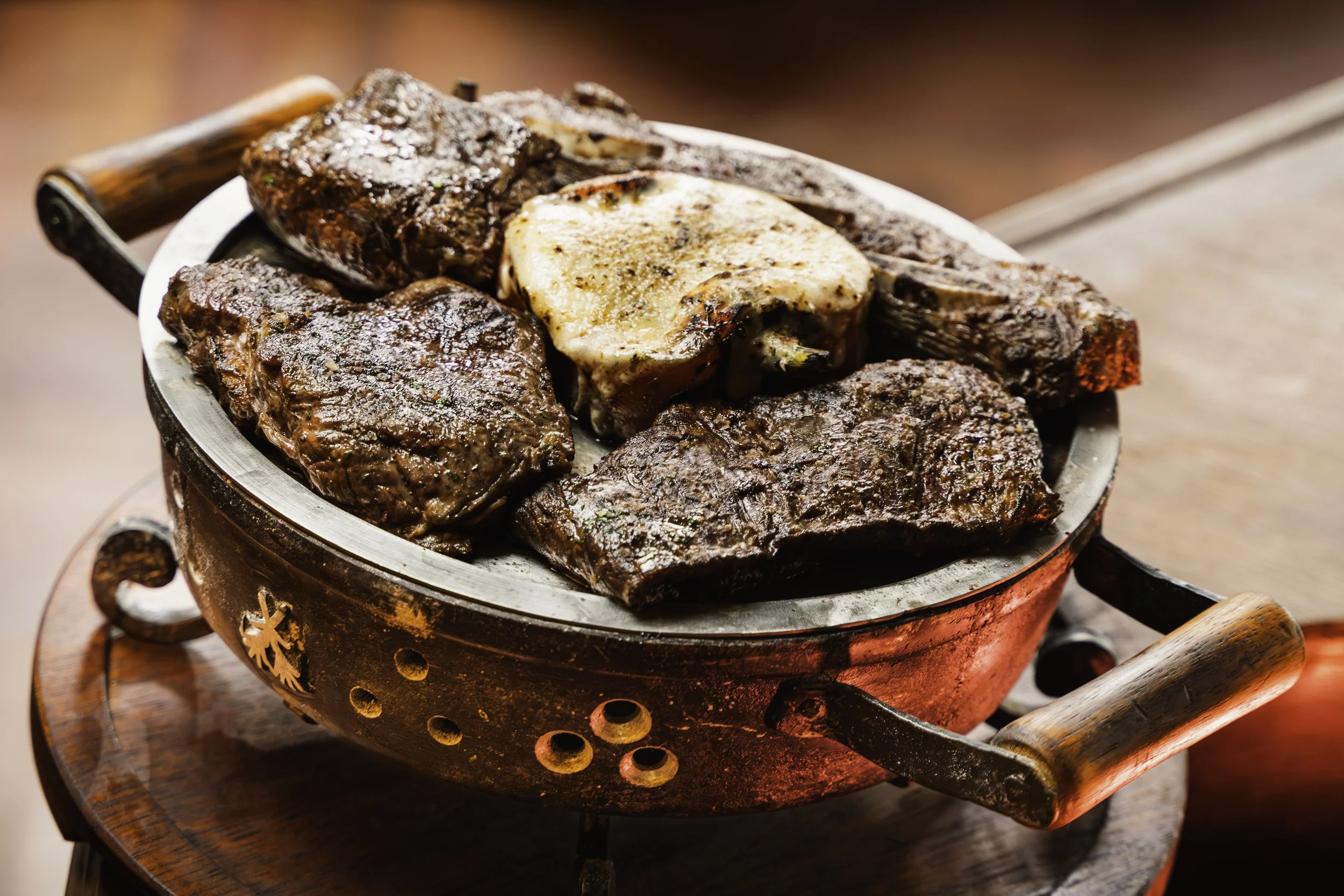 Carne asada y pollo en una cazuela de metal caliente con mango de madera.