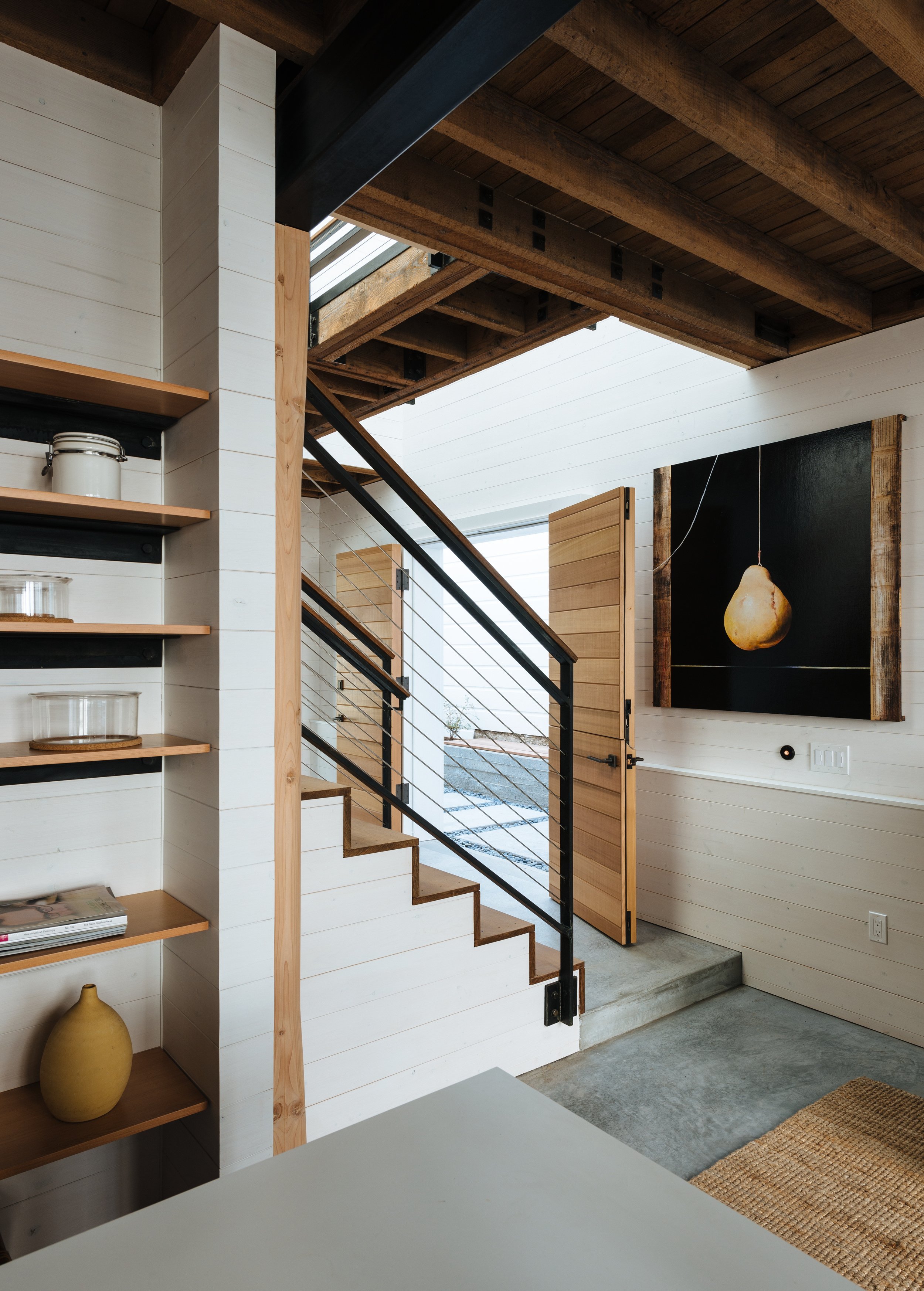 Interior of a modern home with a staircase, open door, artwork, and shelves.