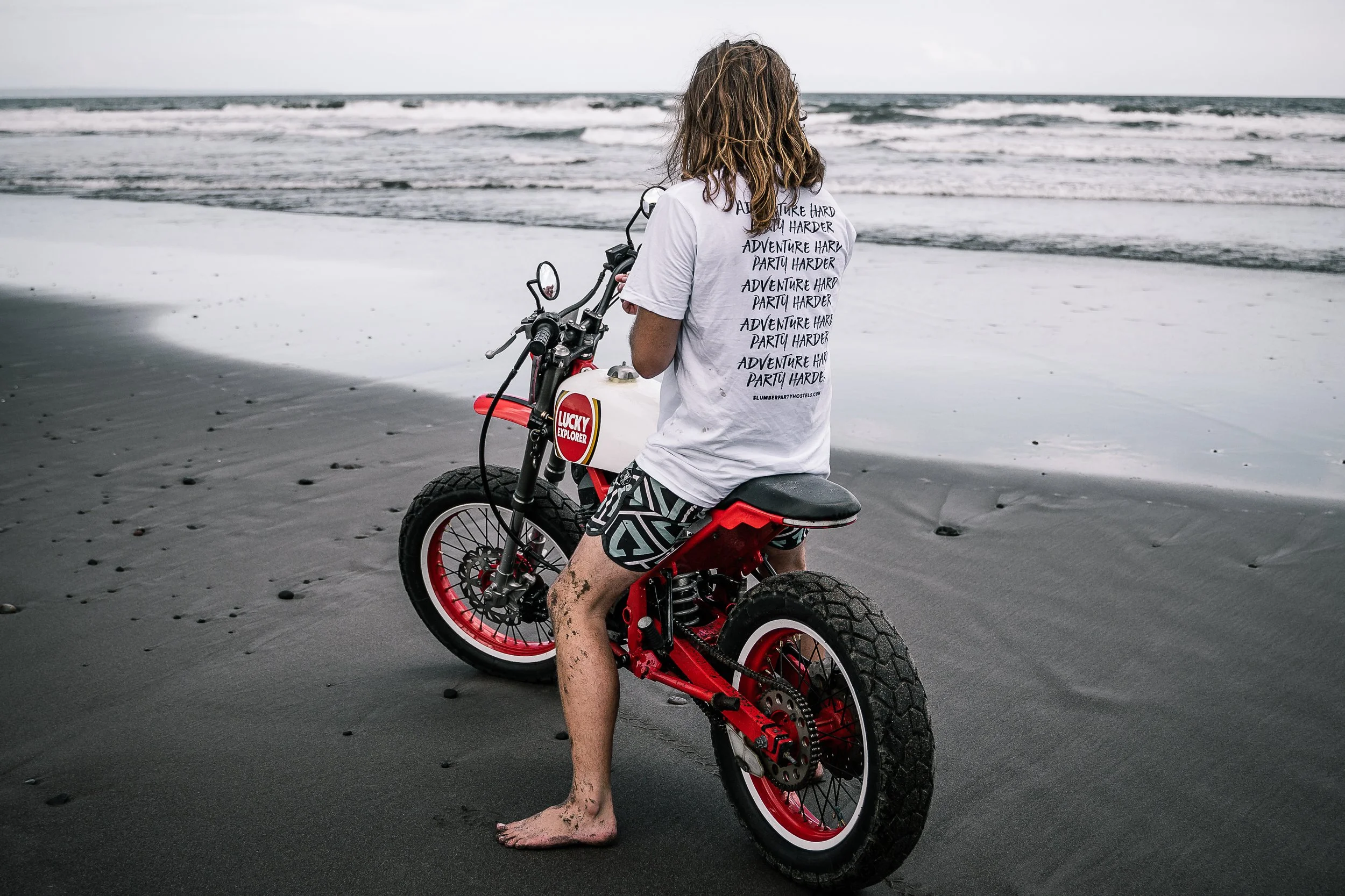 Long-haired barefoot man sits on motorbike on beach | Edmonton motorcycle photographer DarkShark Media