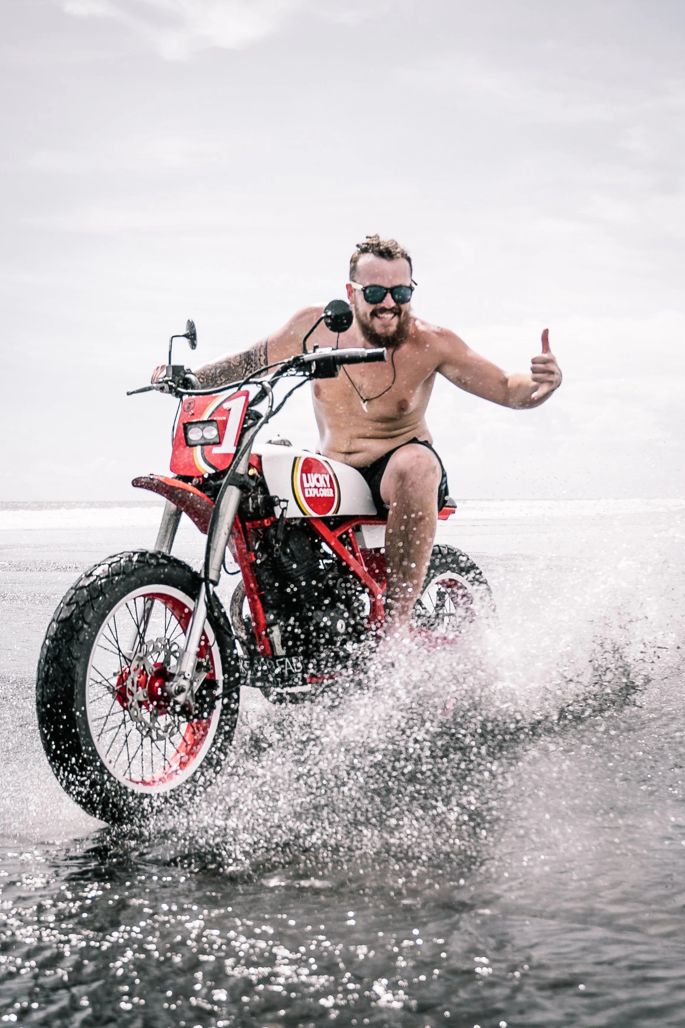 Shirtless man gives a 'hang loose' hand gesture to the camera as he rides motorbike through the water | Edmonton motorcycle photographer DarkShark Media