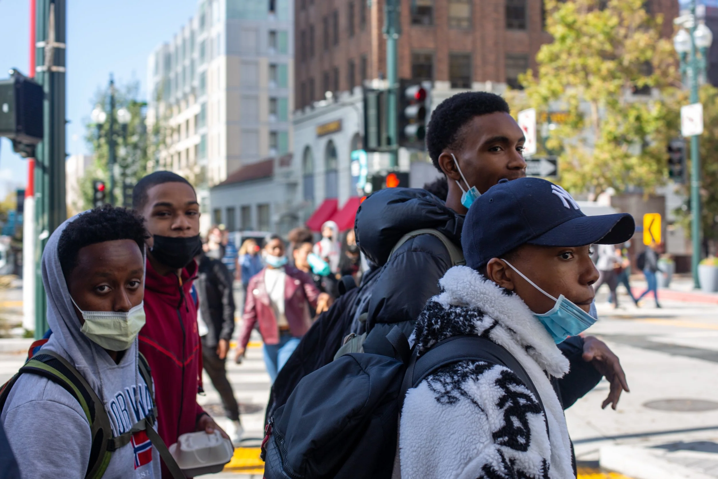A group of four young men wearing masks crossing a busy city street.