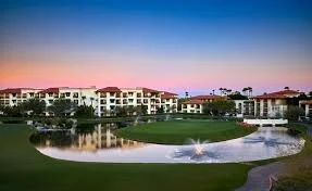 A modern residential complex with white buildings and a golf course with a water feature during sunset.